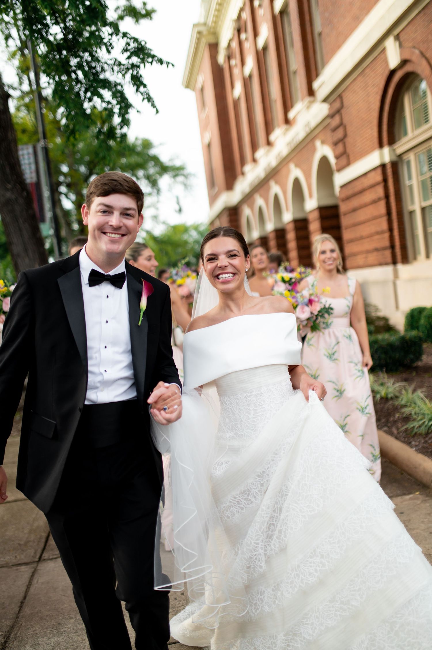 Happy newlyweds walking hand-in-hand outside historic brick building after wedding ceremony.