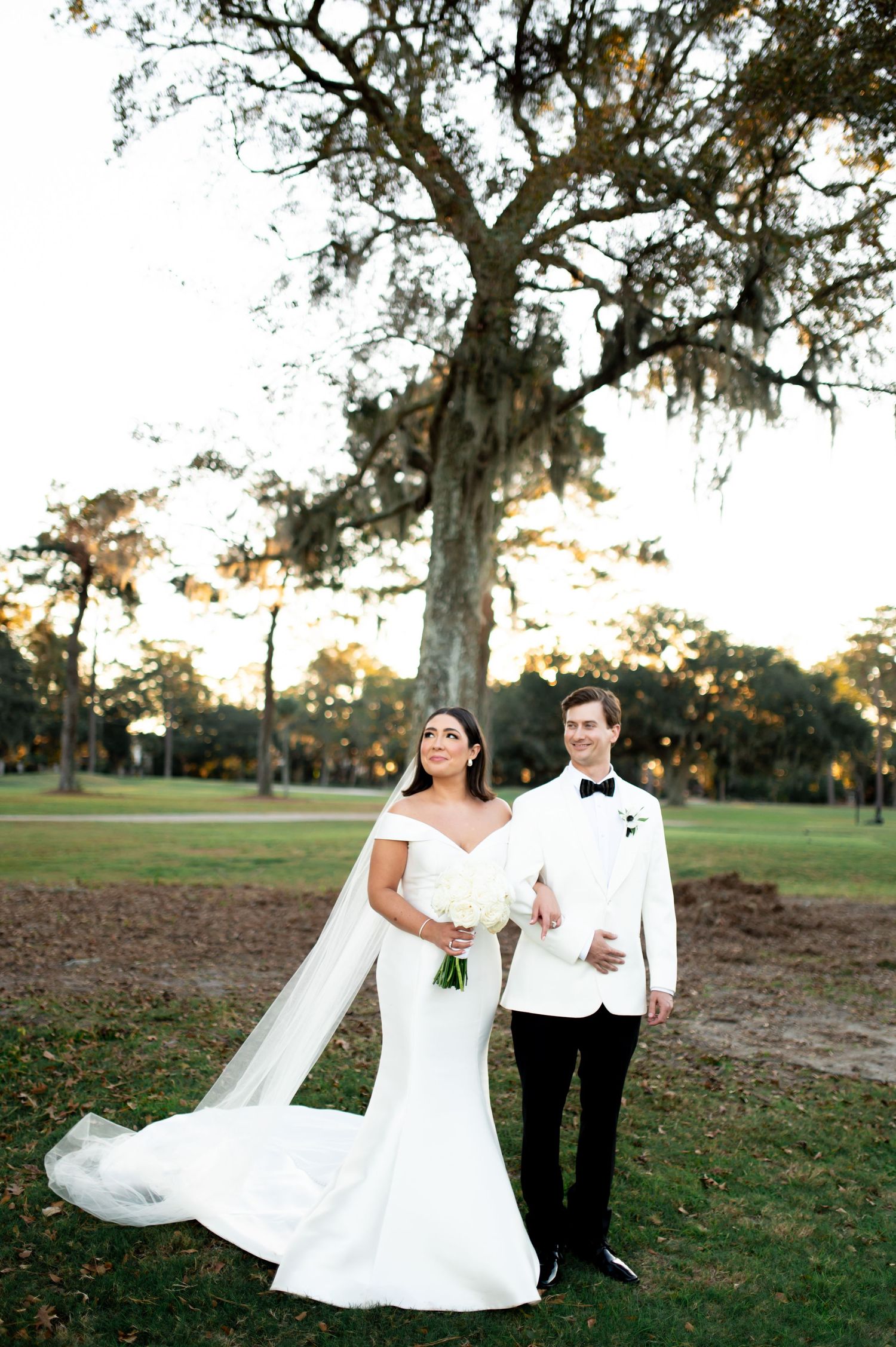 Romantic outdoor wedding photo session in a park with white dress and tuxedo at sunset.