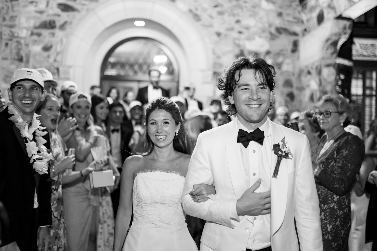 Wedding guests celebrating and walking through a stone archway.