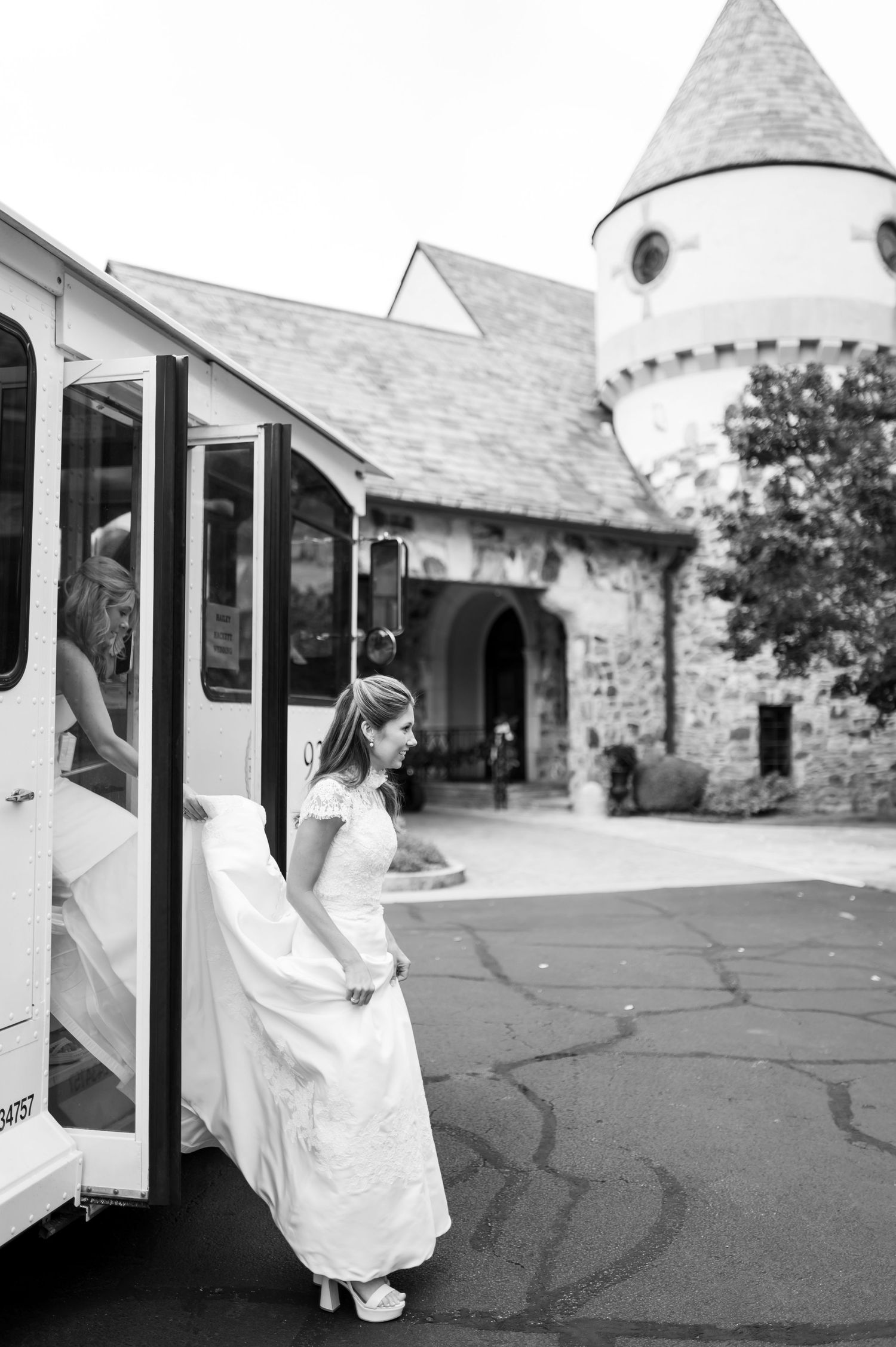 Bride stepping into white wedding shuttle outside stone chapel.