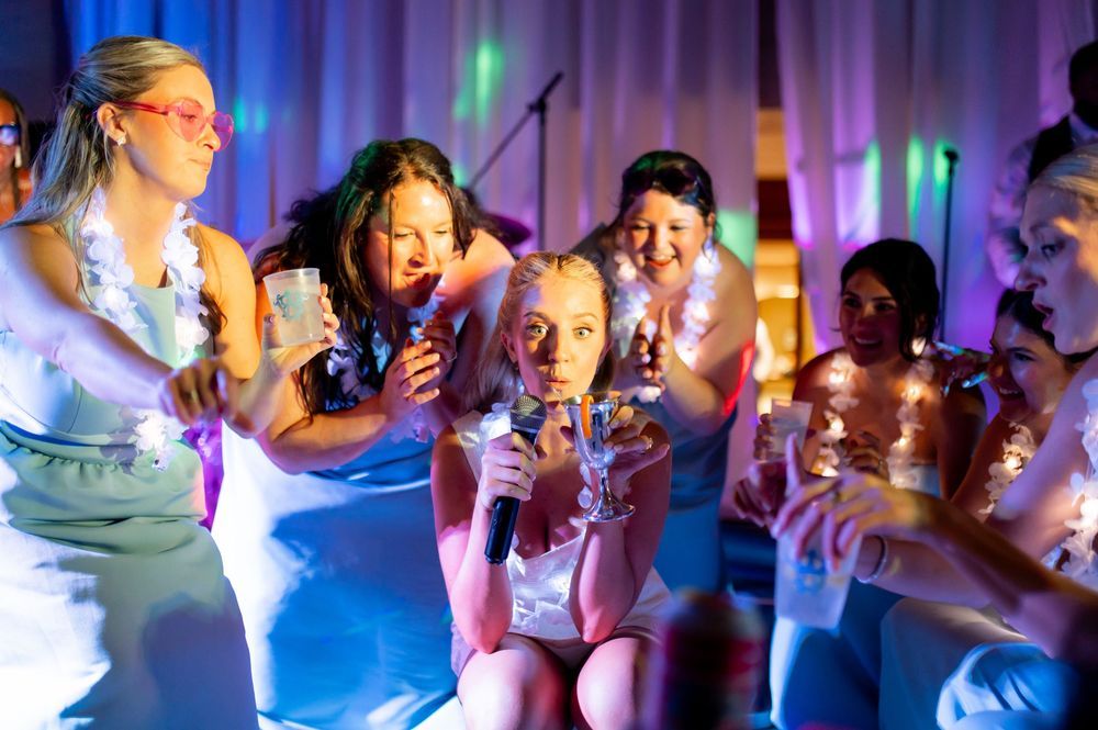 Girls singing karaoke with microphone at colorful party with purple and blue lighting.