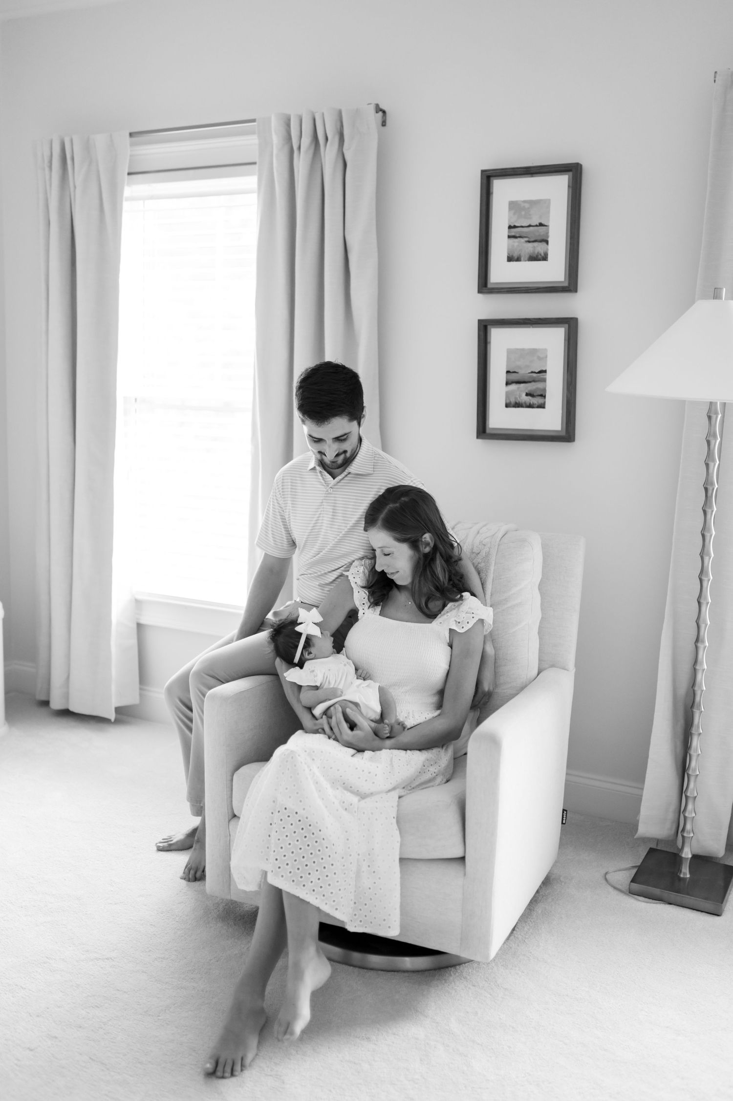 A tender black and white nursery moment with a family gathered in a white armchair by a window.
