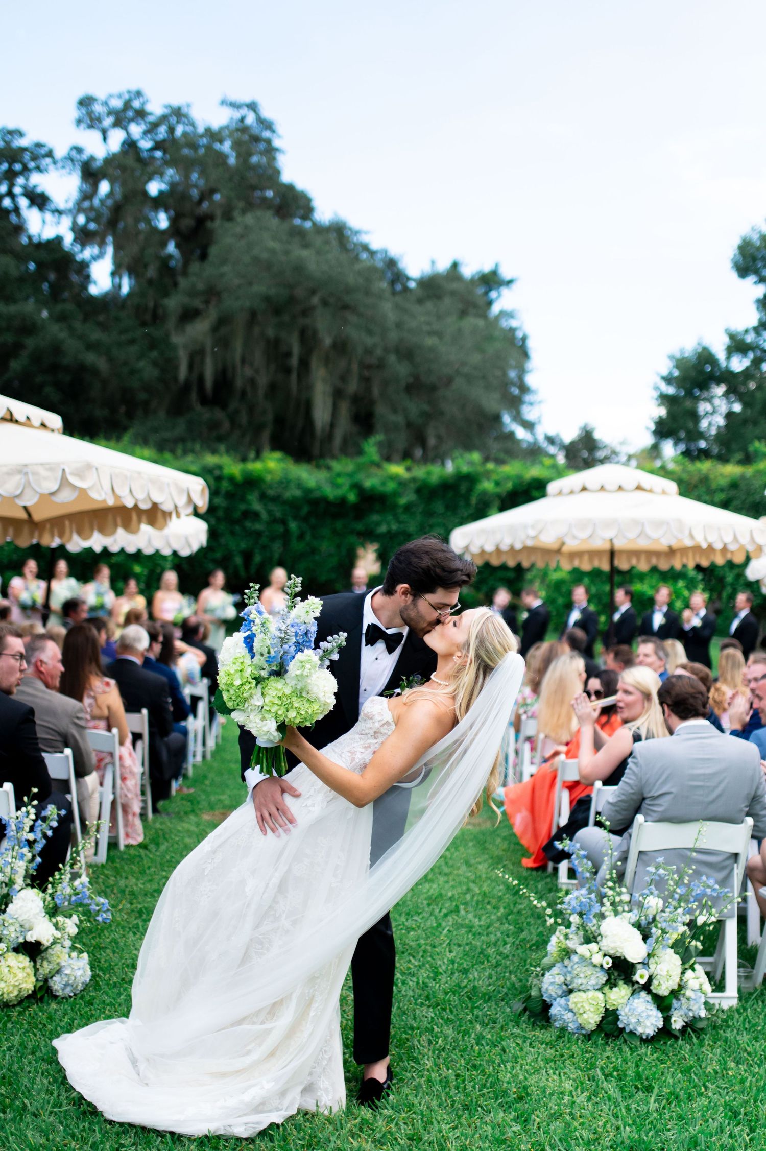Outdoor garden wedding ceremony with white parasols and floral arrangements.