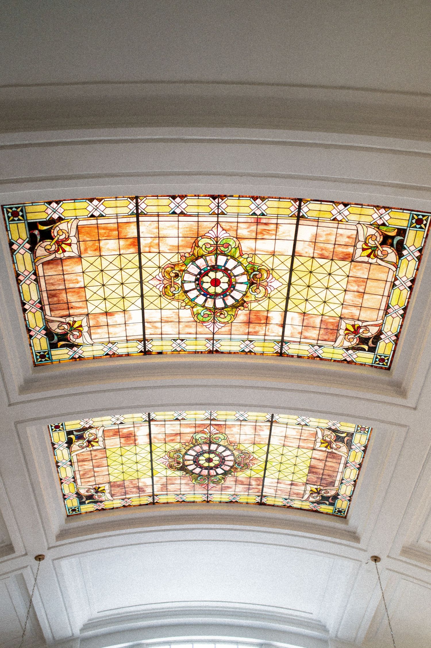 Ornate stained glass skylight ceiling with colorful geometric patterns and floral medallions in a grand architectural interior.
