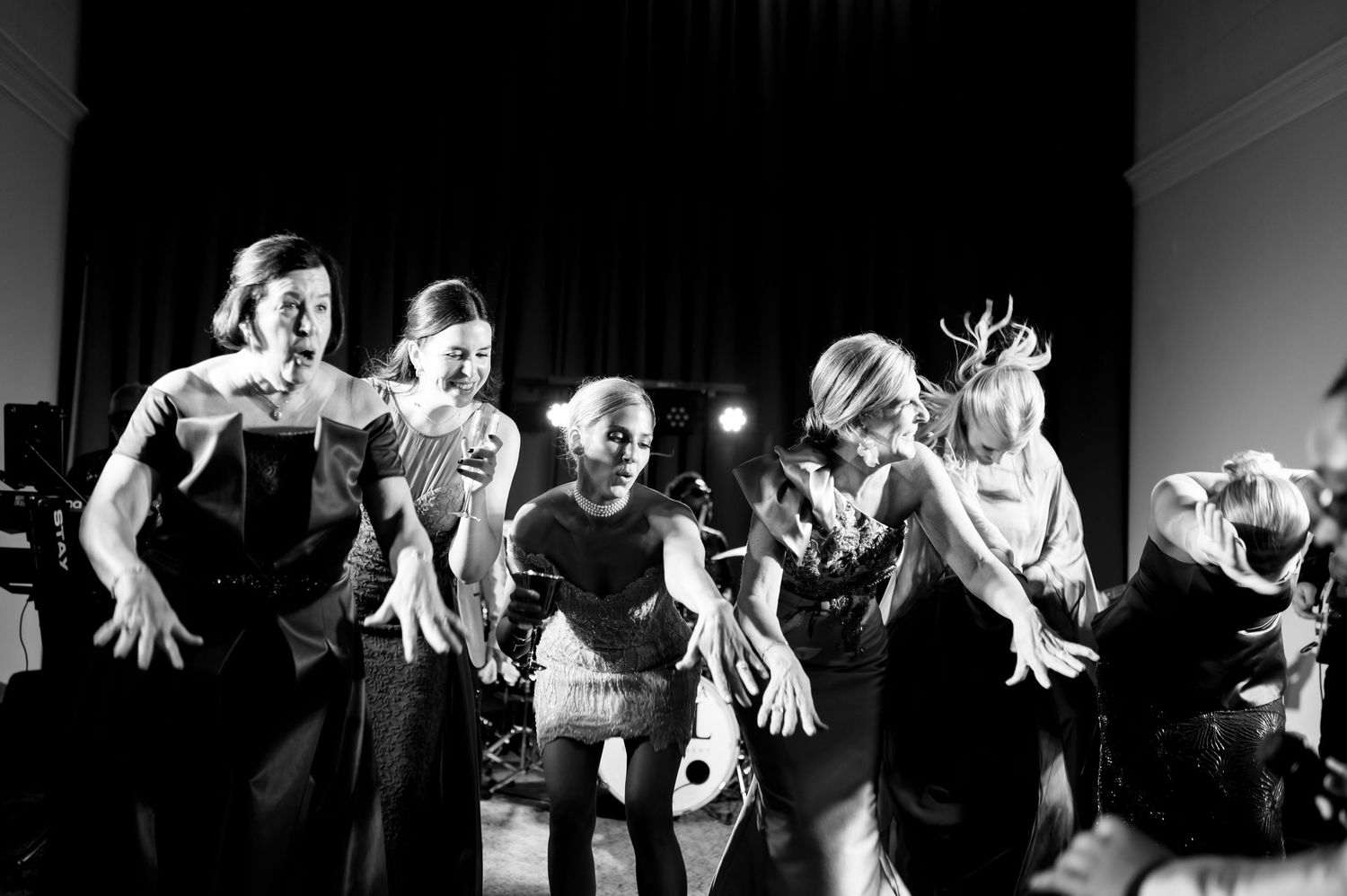 Wedding reception guests dancing and celebrating with raised hands in black and white.
