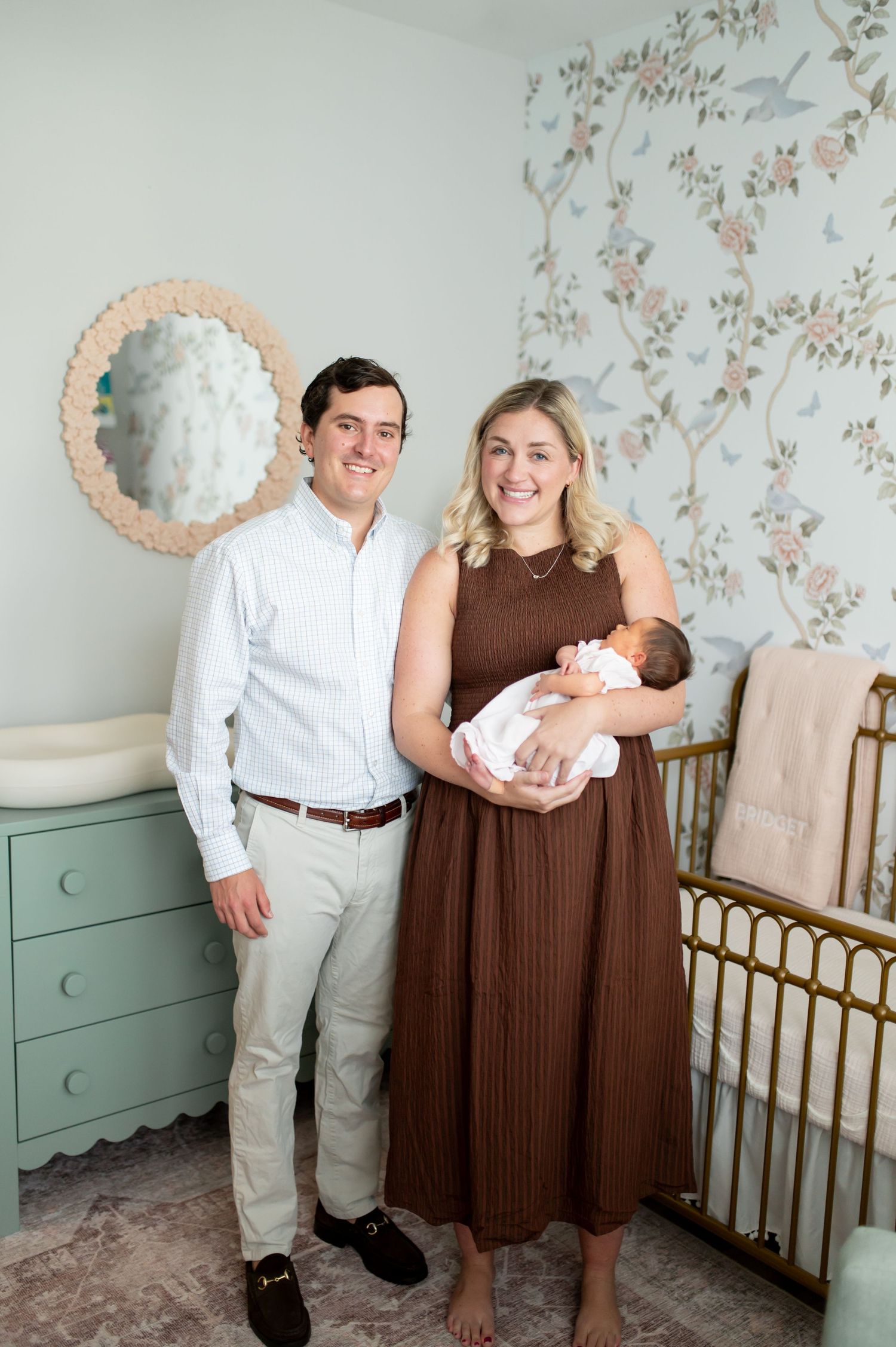 Nursery room with floral wallpaper features vintage-style brass crib and mint green furniture.