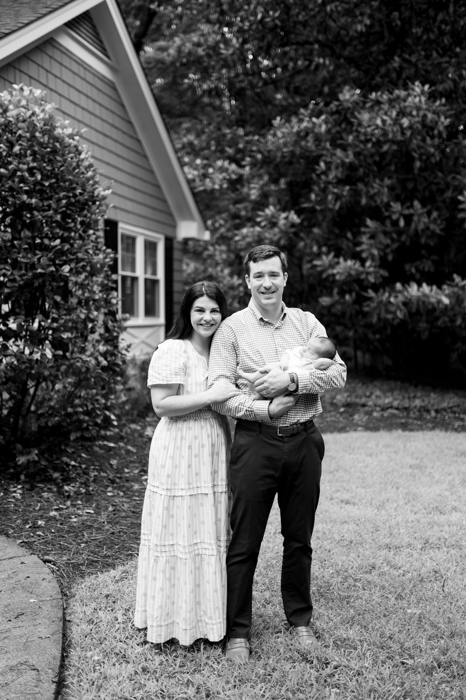 A black and white outdoor portrait of a family standing together in front of their house.