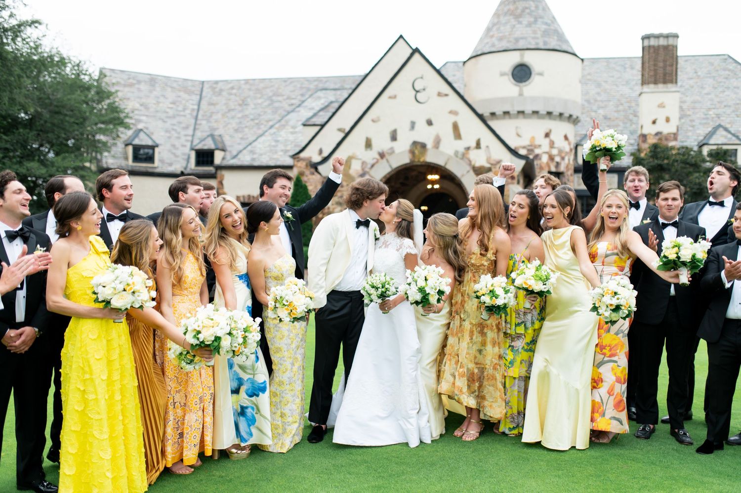 Large wedding party in yellow dresses and formal attire pose outdoors by stone church.