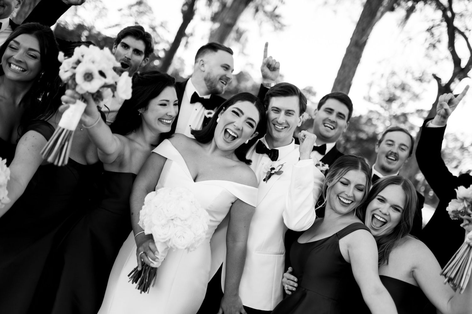 Wedding party in black and white attire celebrates joyfully during outdoor photo session.
