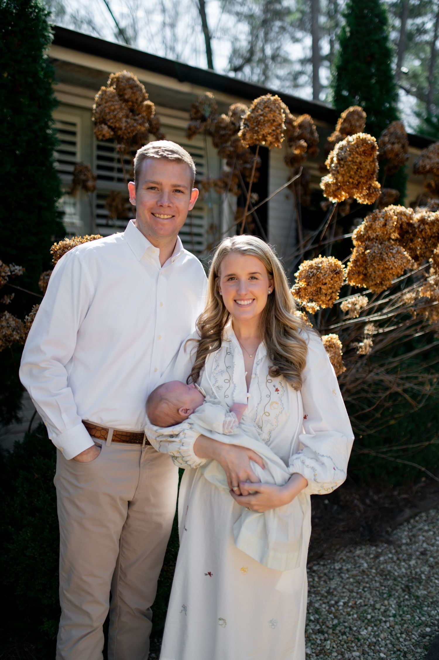 A family photo session in winter features matching white outfits against a backdrop of dried hydrangea blooms.
