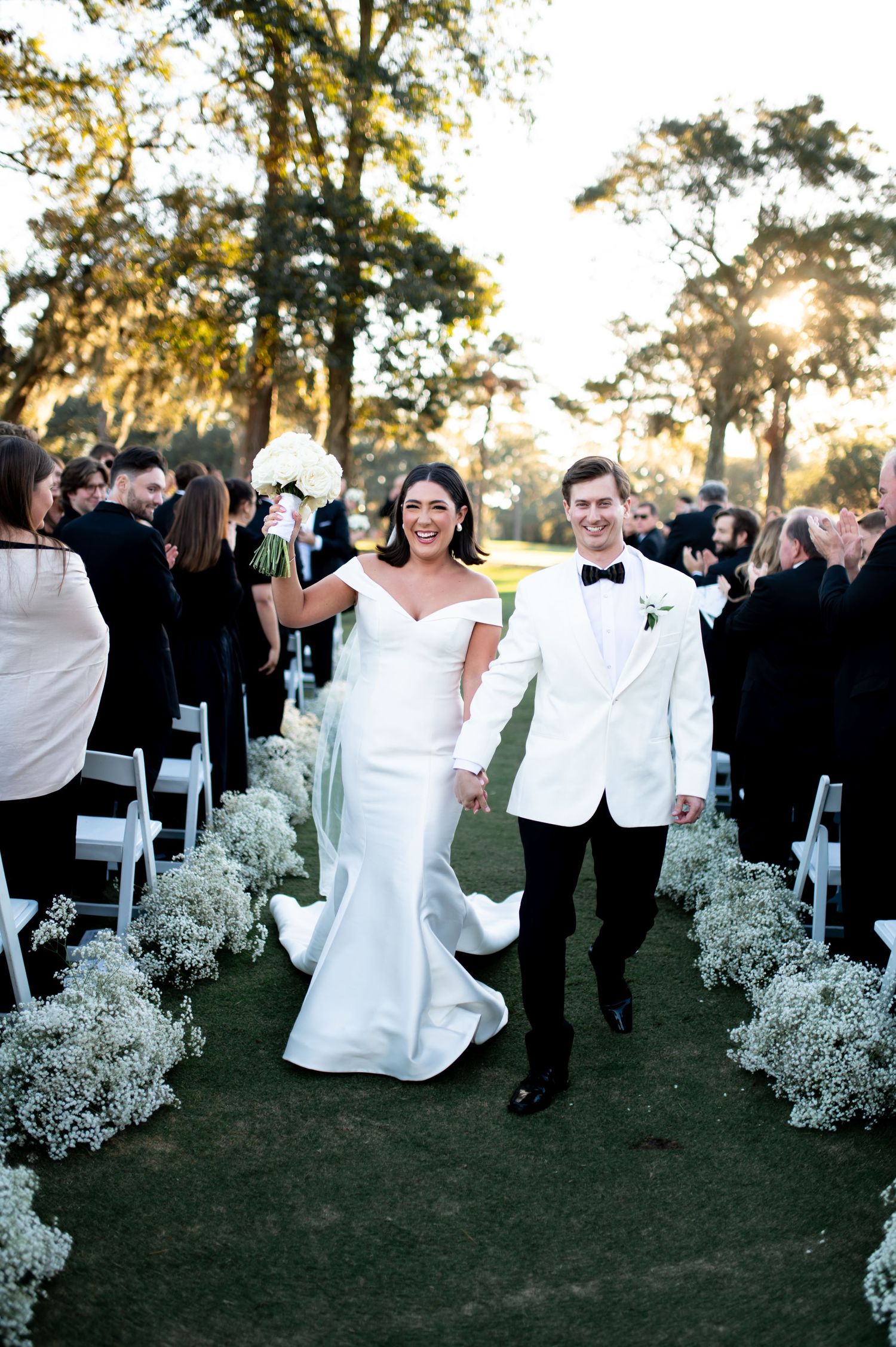 Wedding celebration with guests dancing outdoors surrounded by baby's breath floral decorations at sunset.