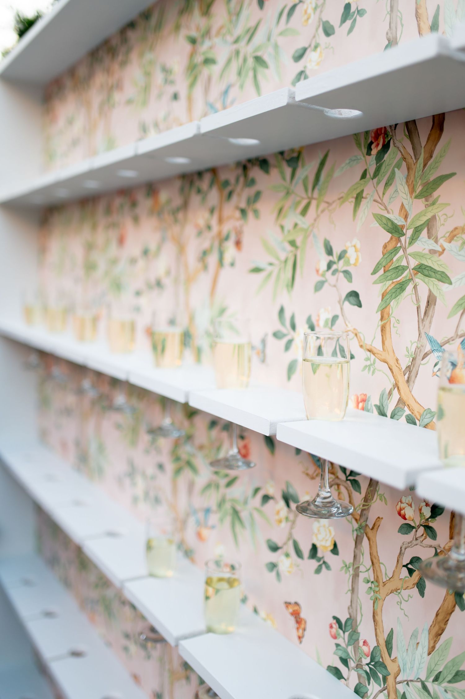 Elegant white shelving against floral wallpaper with delicate botanical pattern.