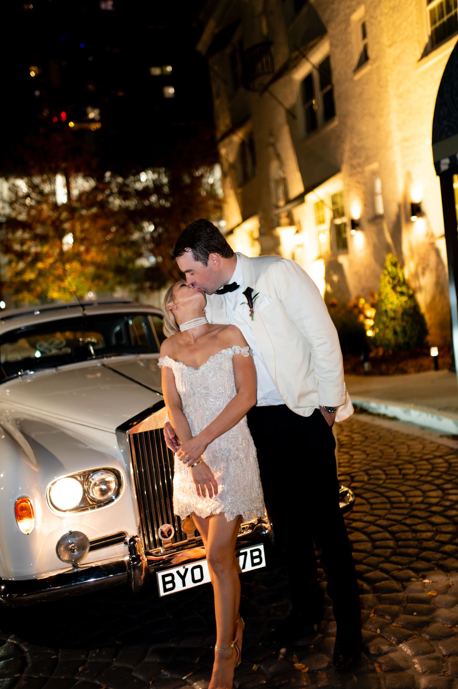 Romantic nighttime photo shoot with a classic white Rolls Royce on cobblestone street.