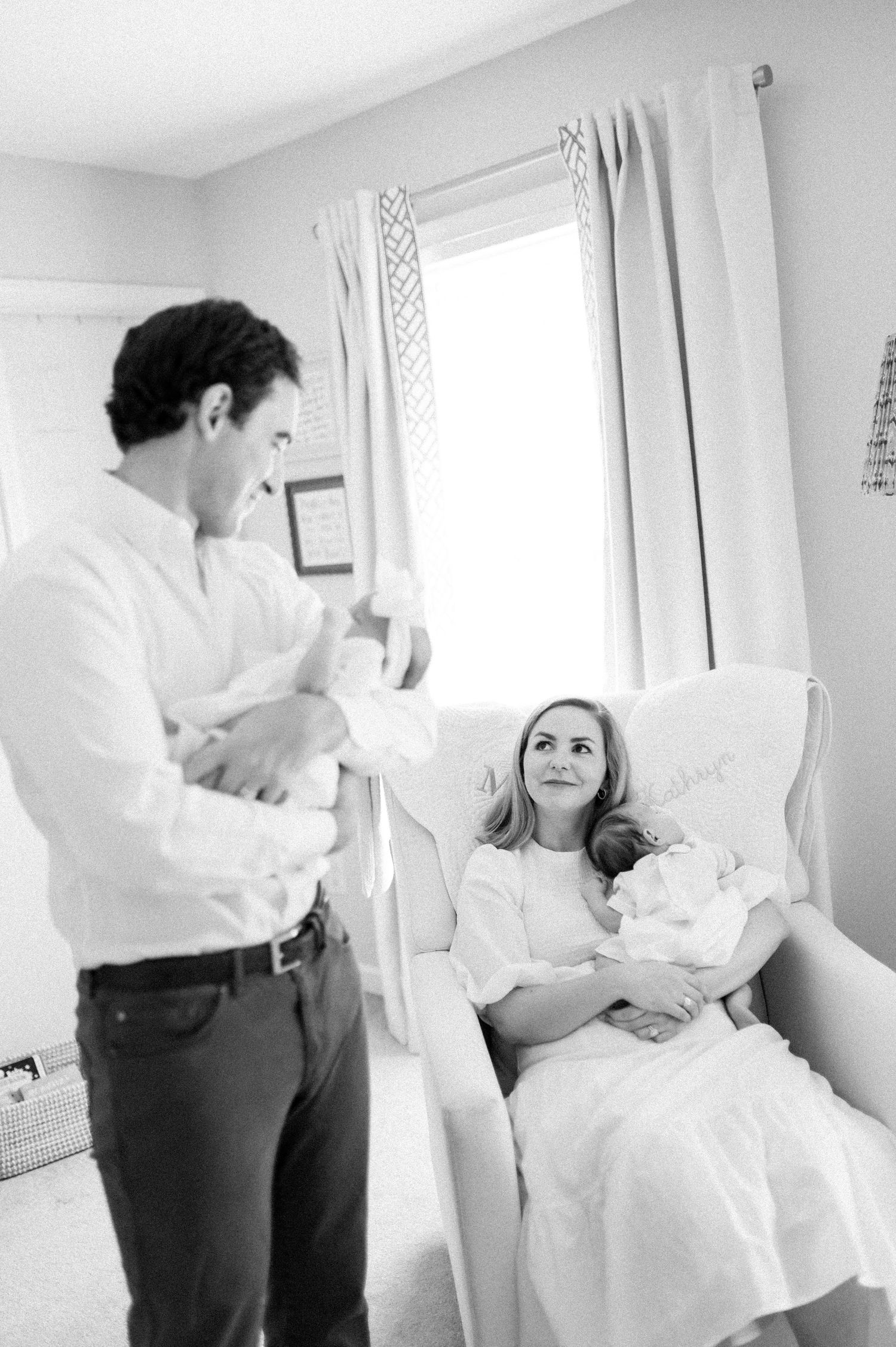 Black and white photo of new parents holding their newborn baby in a nursery room.