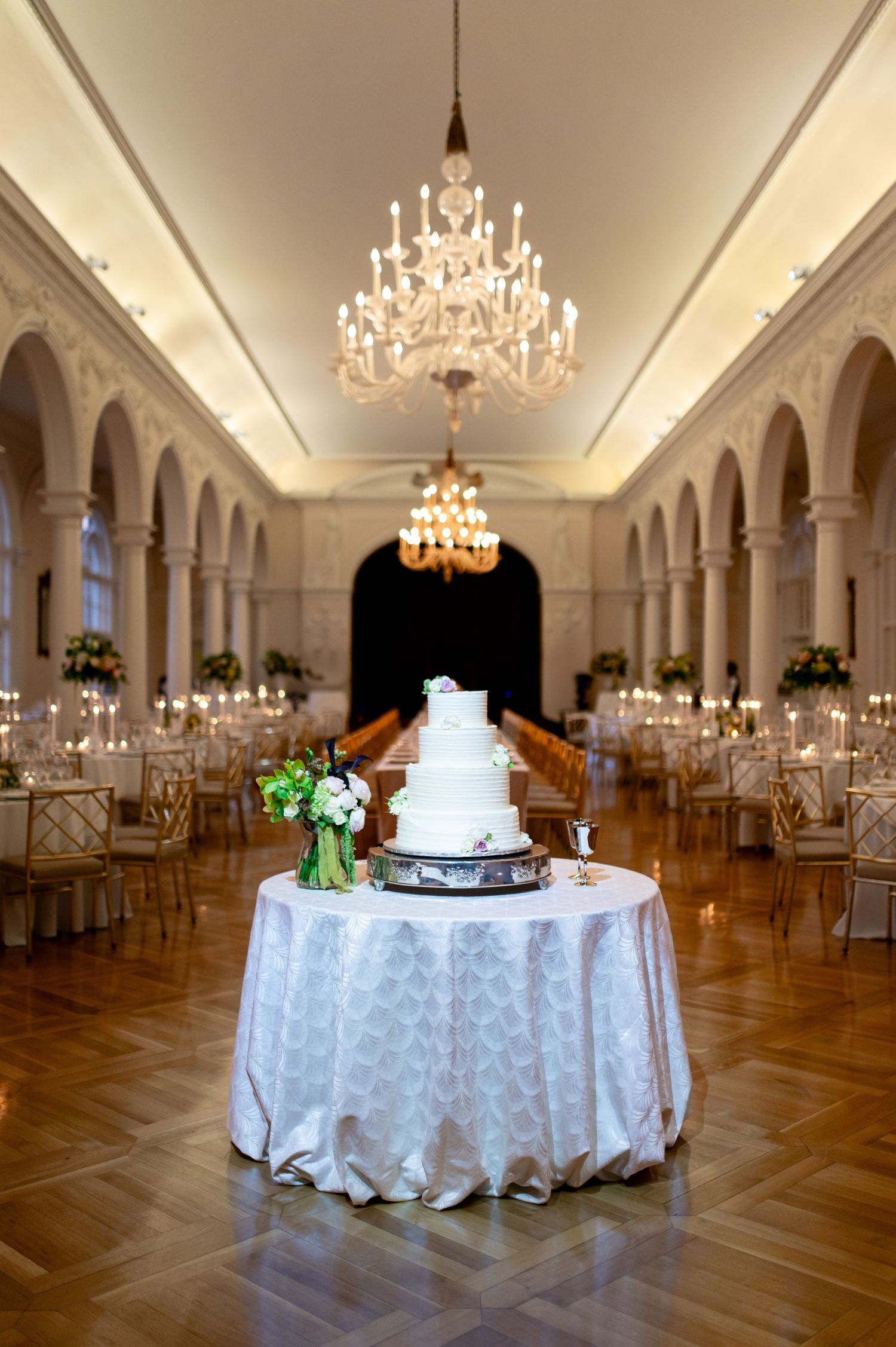 A grand ballroom set for a wedding reception with crystal chandeliers and white table settings.