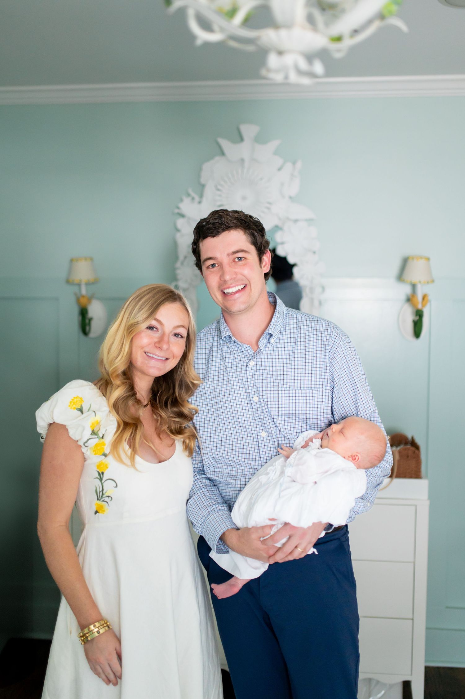 A family poses together in a mint green nursery room with white furniture.