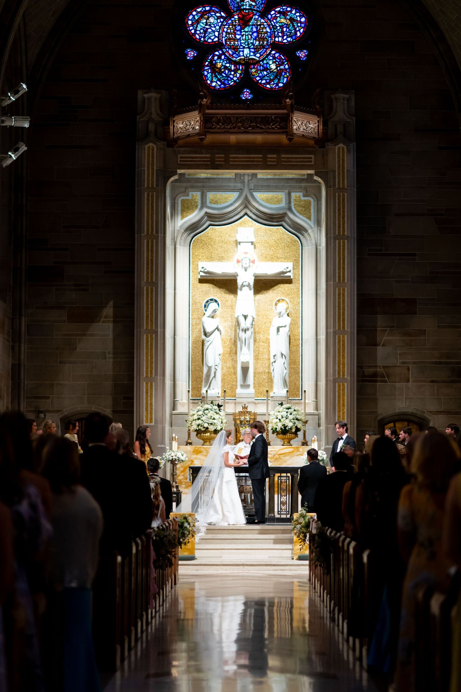 Cathedral wedding ceremony with illuminated altar and crucifix in dramatic lighting.
