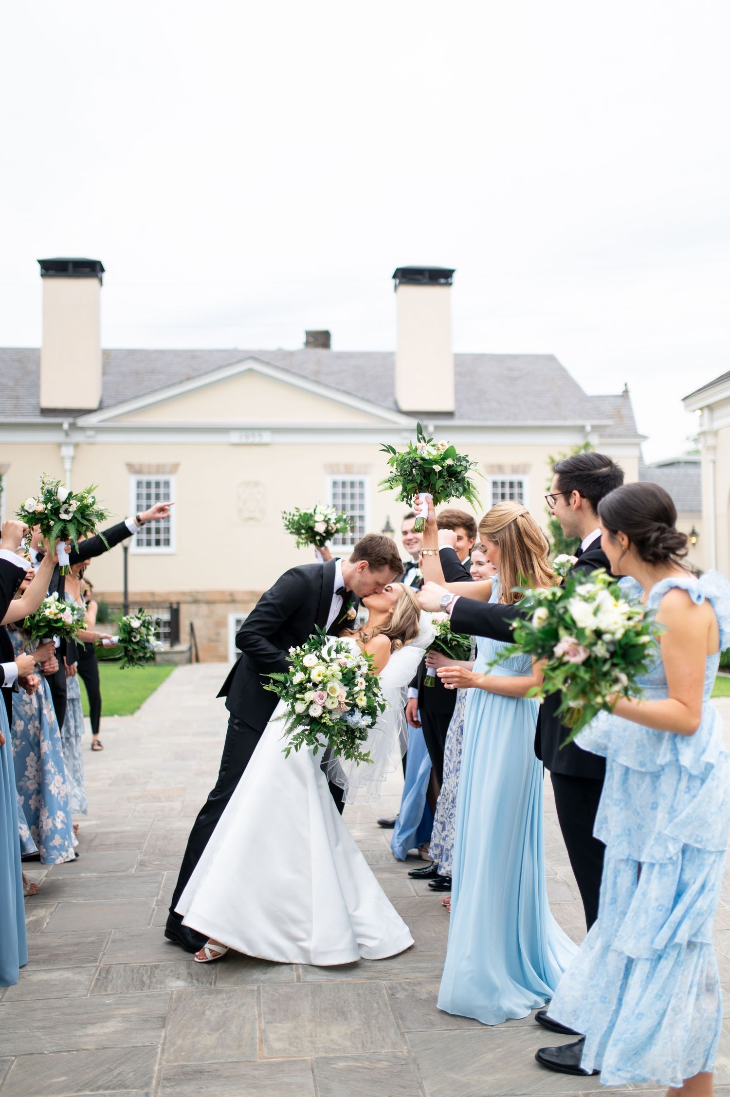 Joyful wedding celebration with bridesmaids in light blue dresses outside a colonial venue.