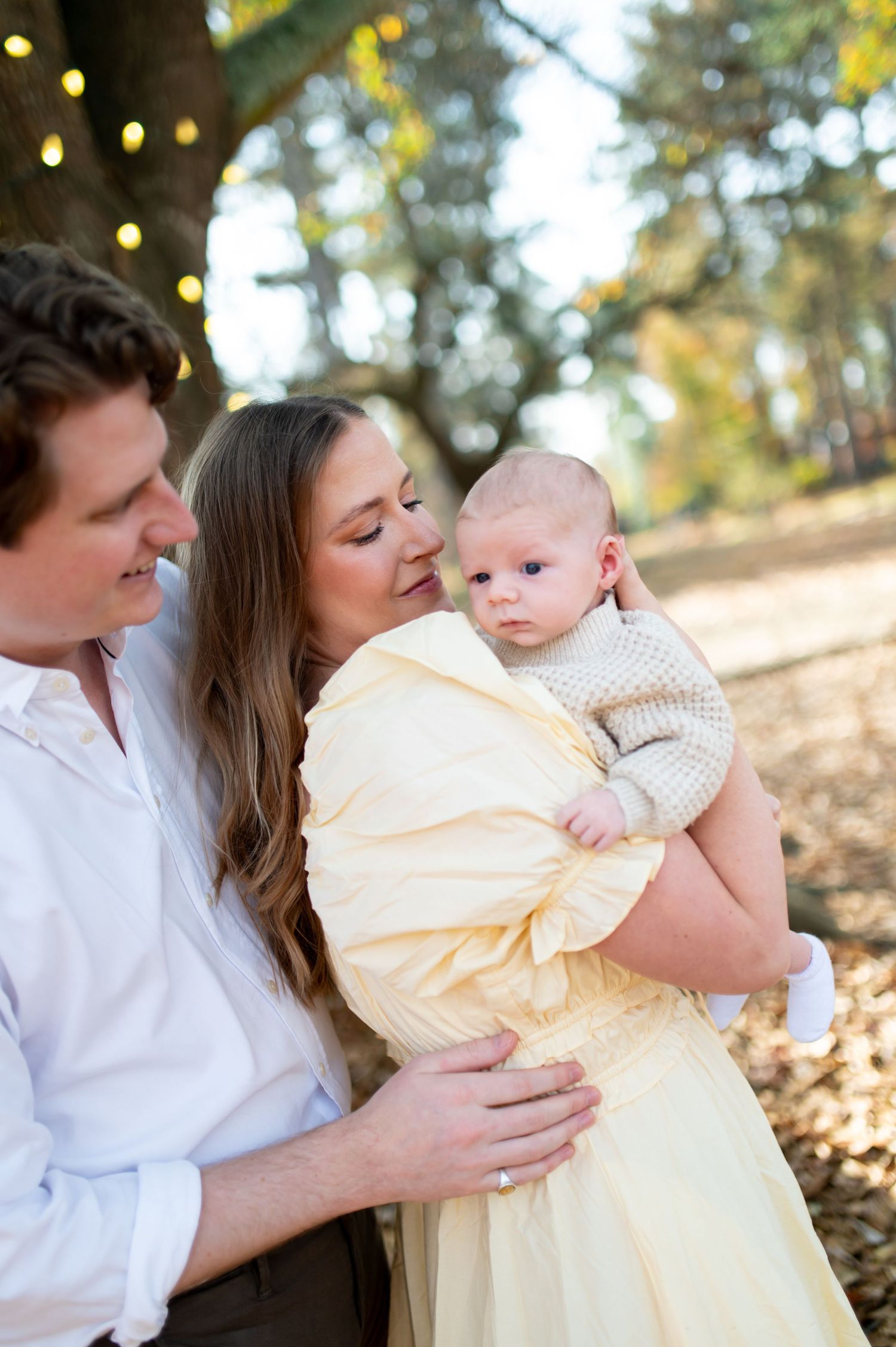 A family shares tender moments together outdoors during a photo session with soft autumn lighting and bokeh effects.