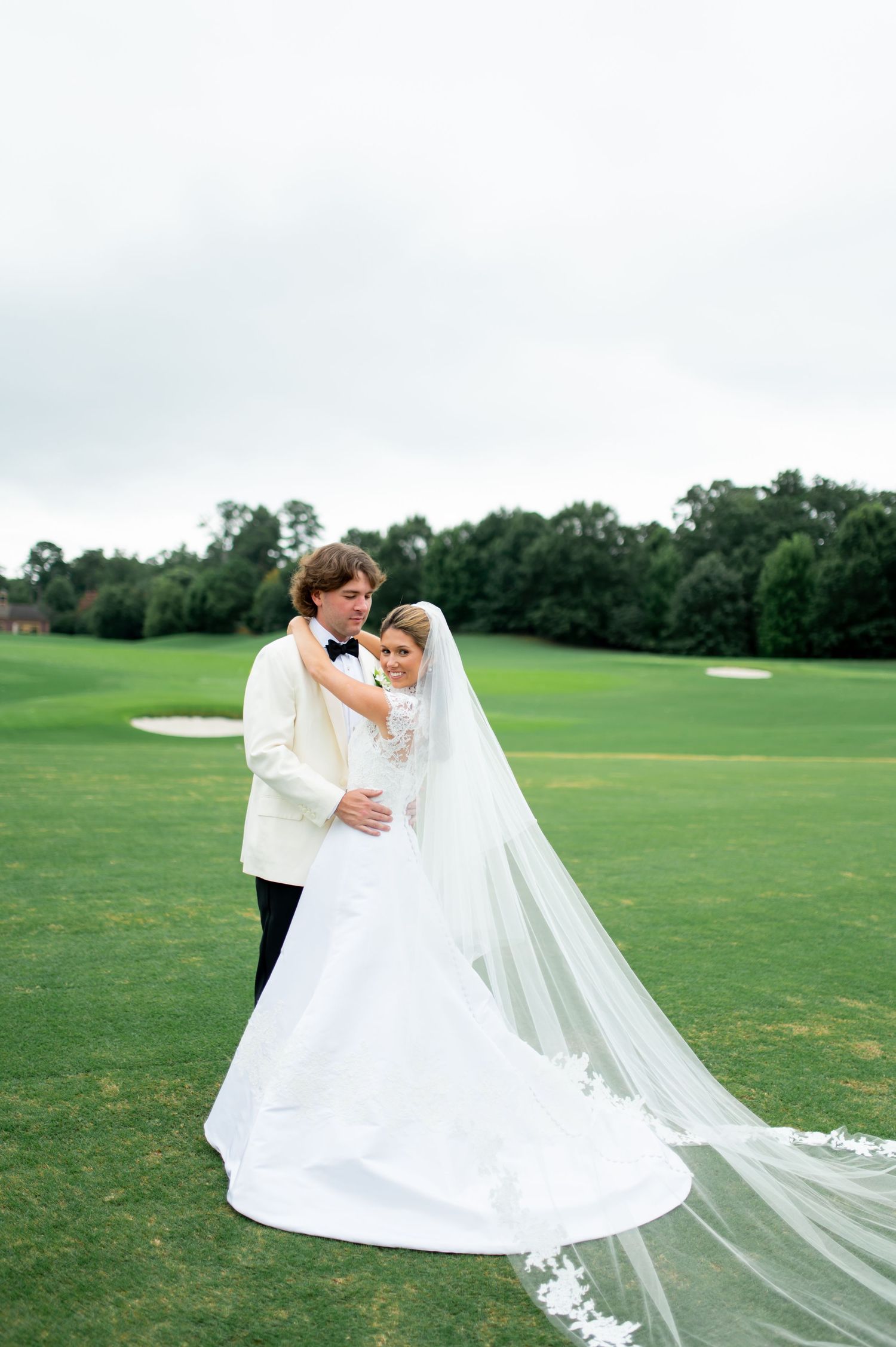 Wedding couple embracing on a golf course with a dramatic flowing veil.