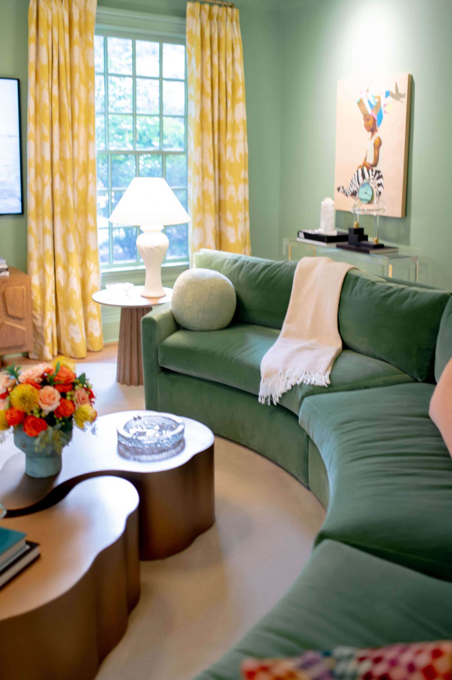 Green curved sectional sofa in a mint-walled living room with yellow curtains and a sculptural gold coffee table.