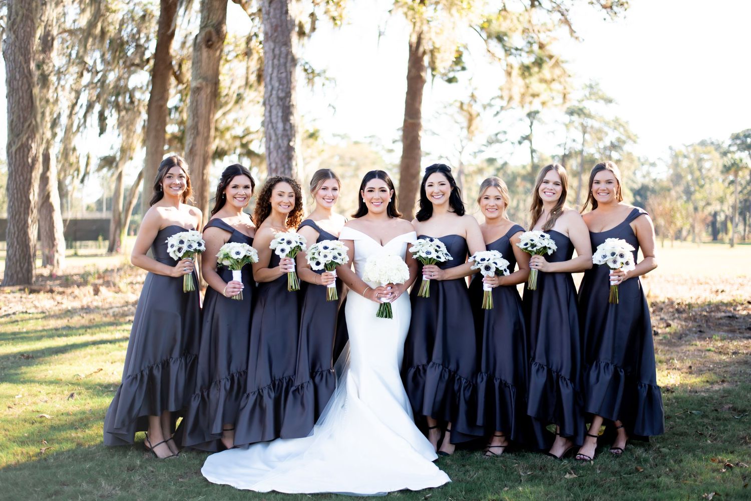Wedding party in navy and white poses together under trees at outdoor ceremony.