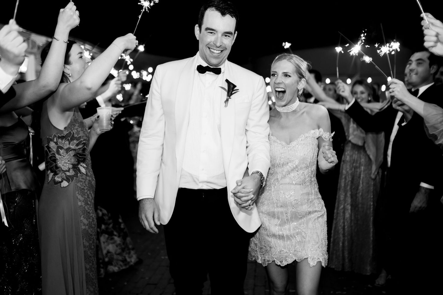 Black and white photo of wedding guests dancing with sparklers at night.