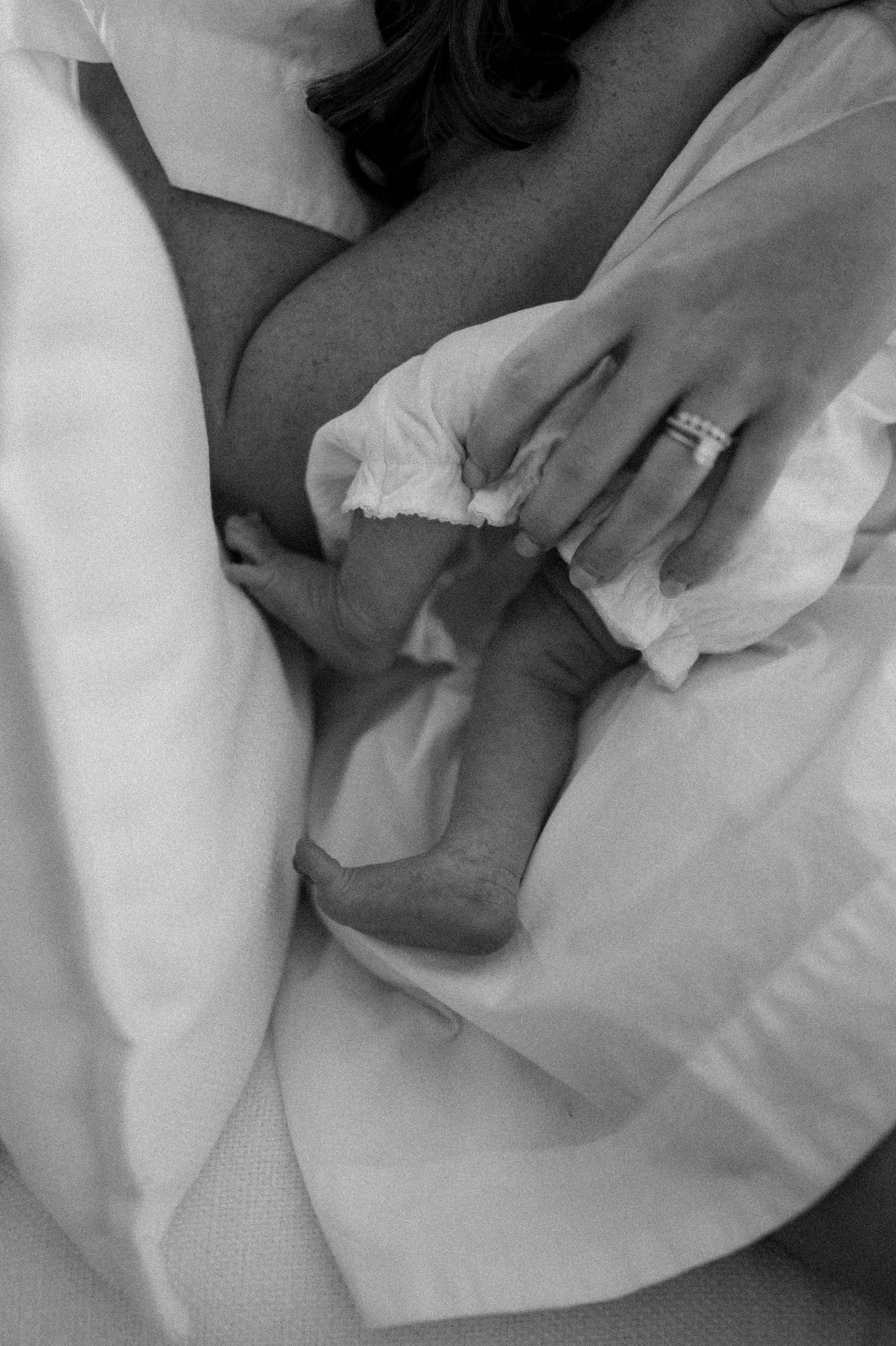 A tender black and white photograph shows a small baby's foot being gently held against white bedding.