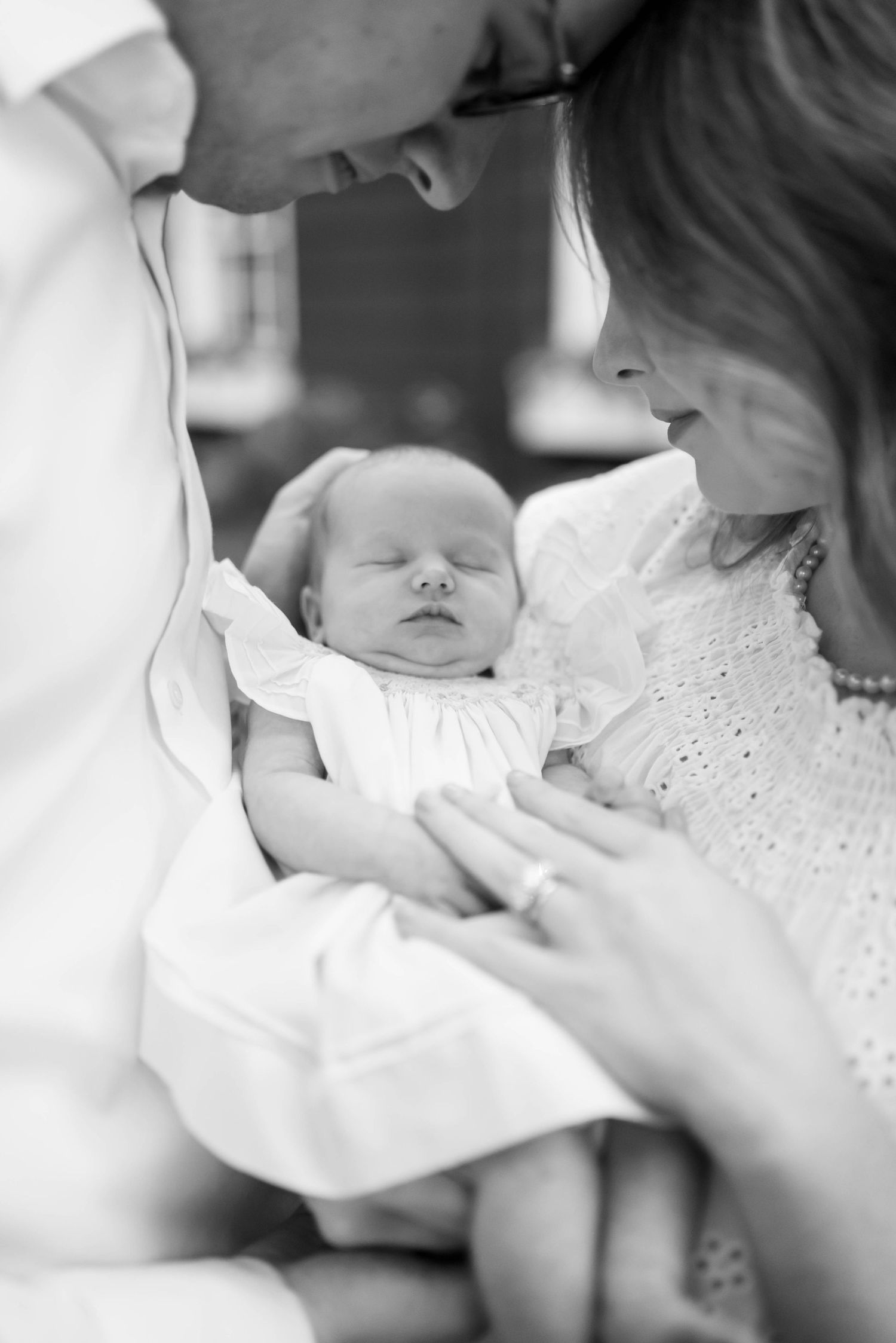 A sleeping newborn baby dressed in white lace is gently cradled.