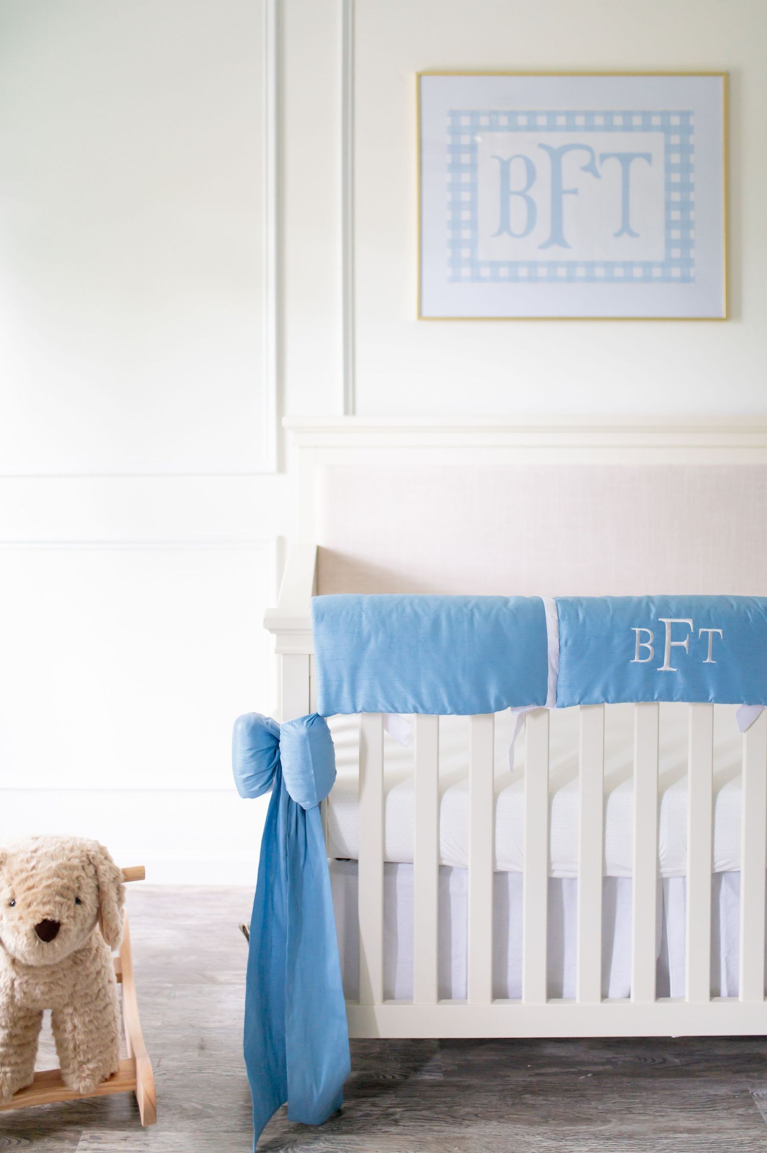 A white nursery crib with blue accents and monogrammed bedding beside a plush toy.