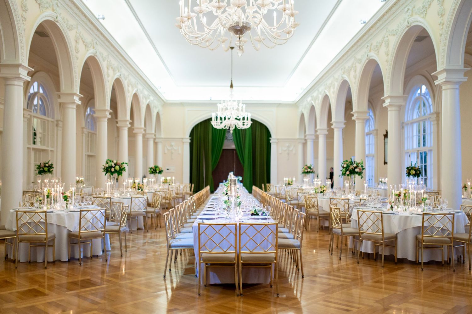 Grand ballroom with crystal chandeliers and white columns set for an elegant wedding reception.