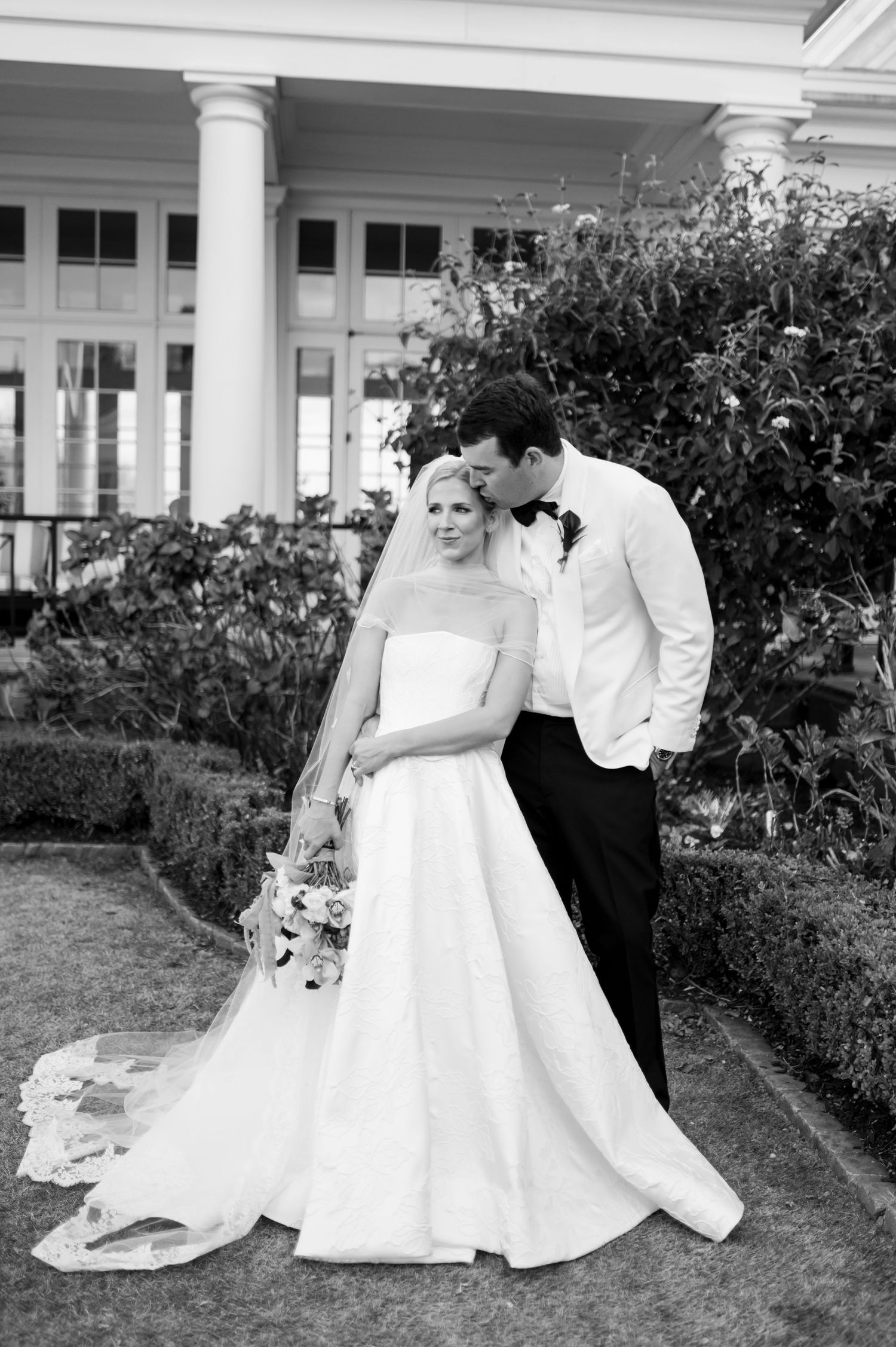 Artistic black and white wedding portraits on a manicured lawn with colonial architecture.