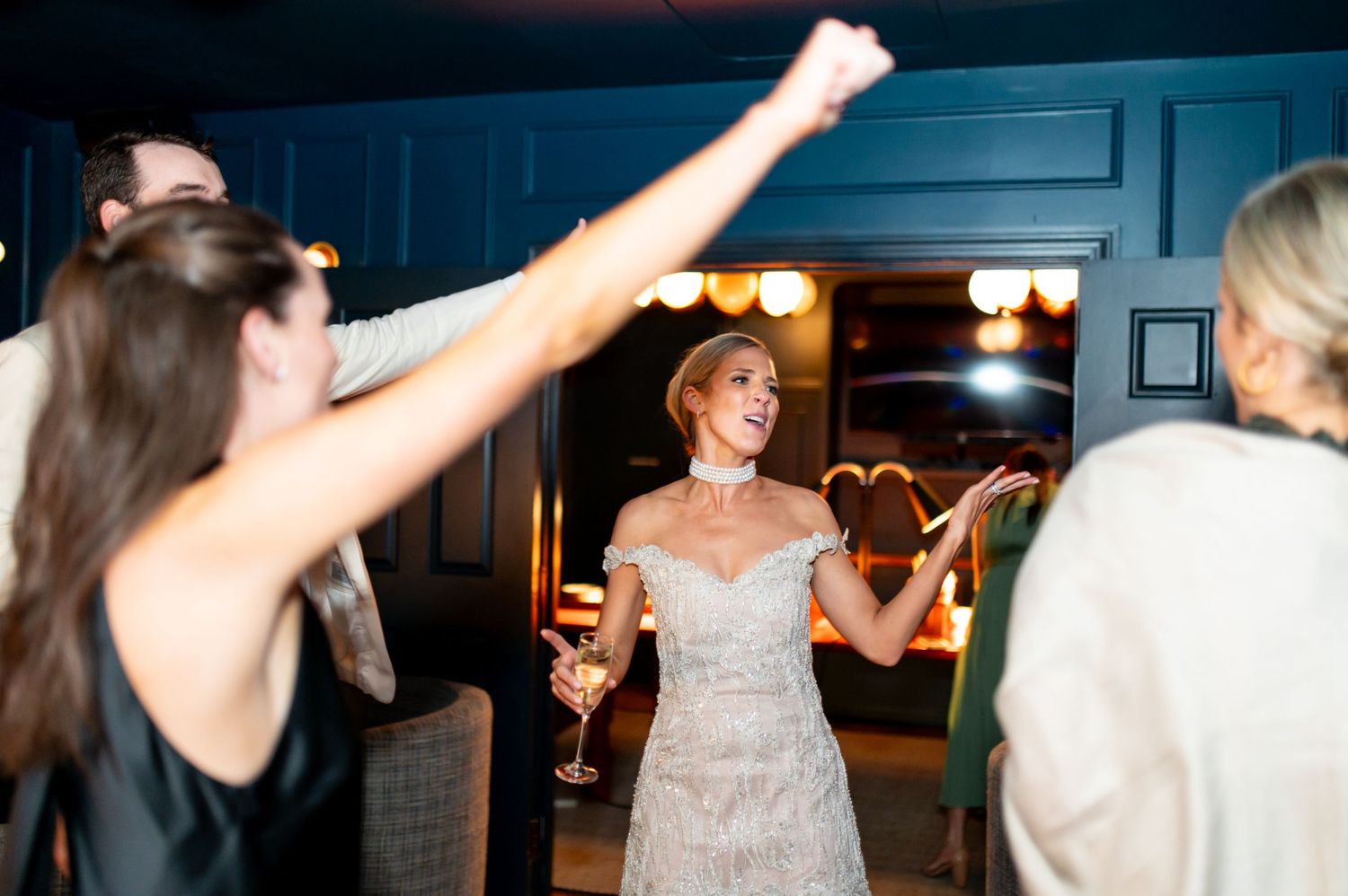 Wedding celebration with people dancing and raising arms in dimly lit venue.