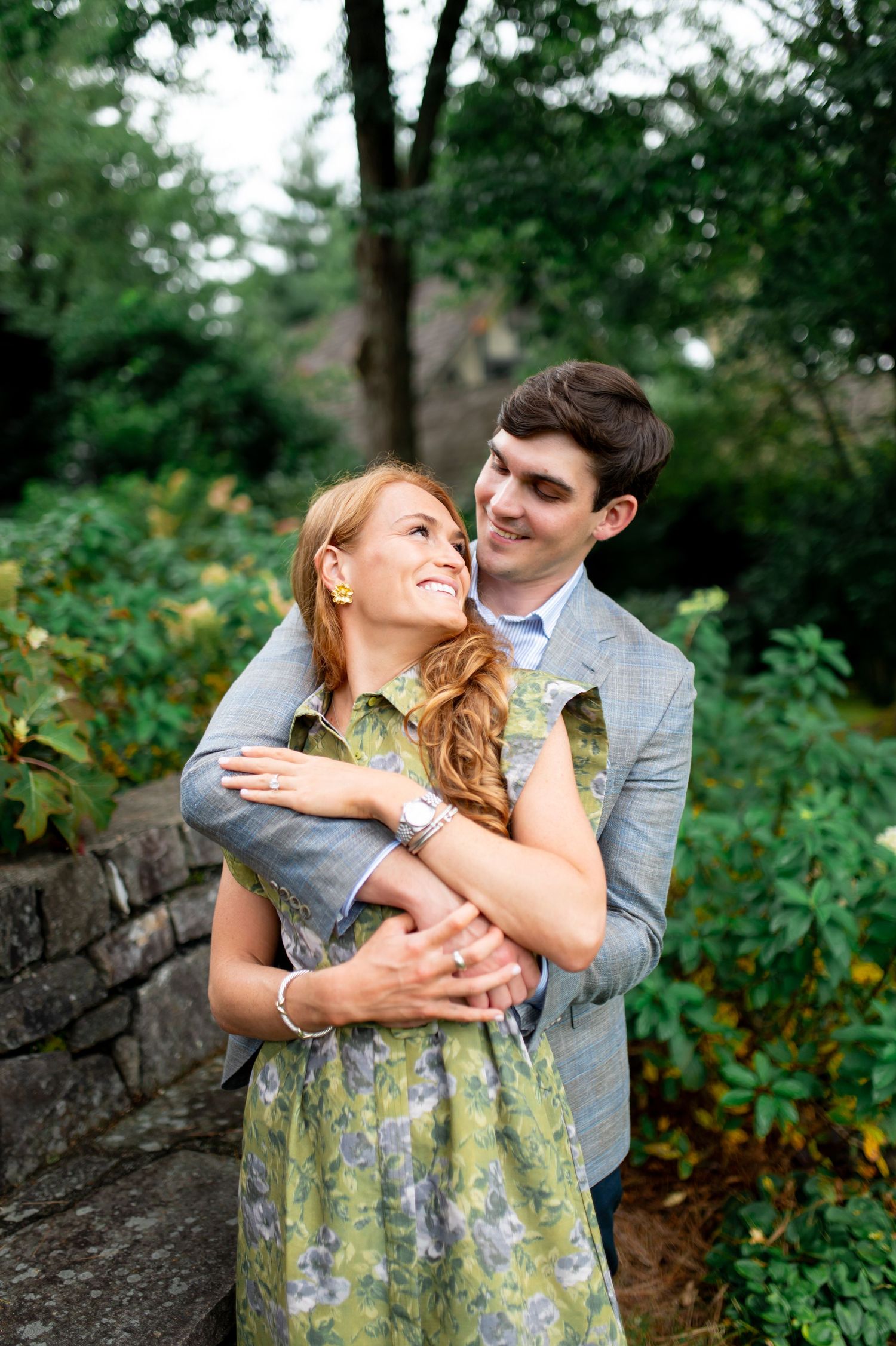 Romantic couple embracing in a garden setting with stone wall and greenery.