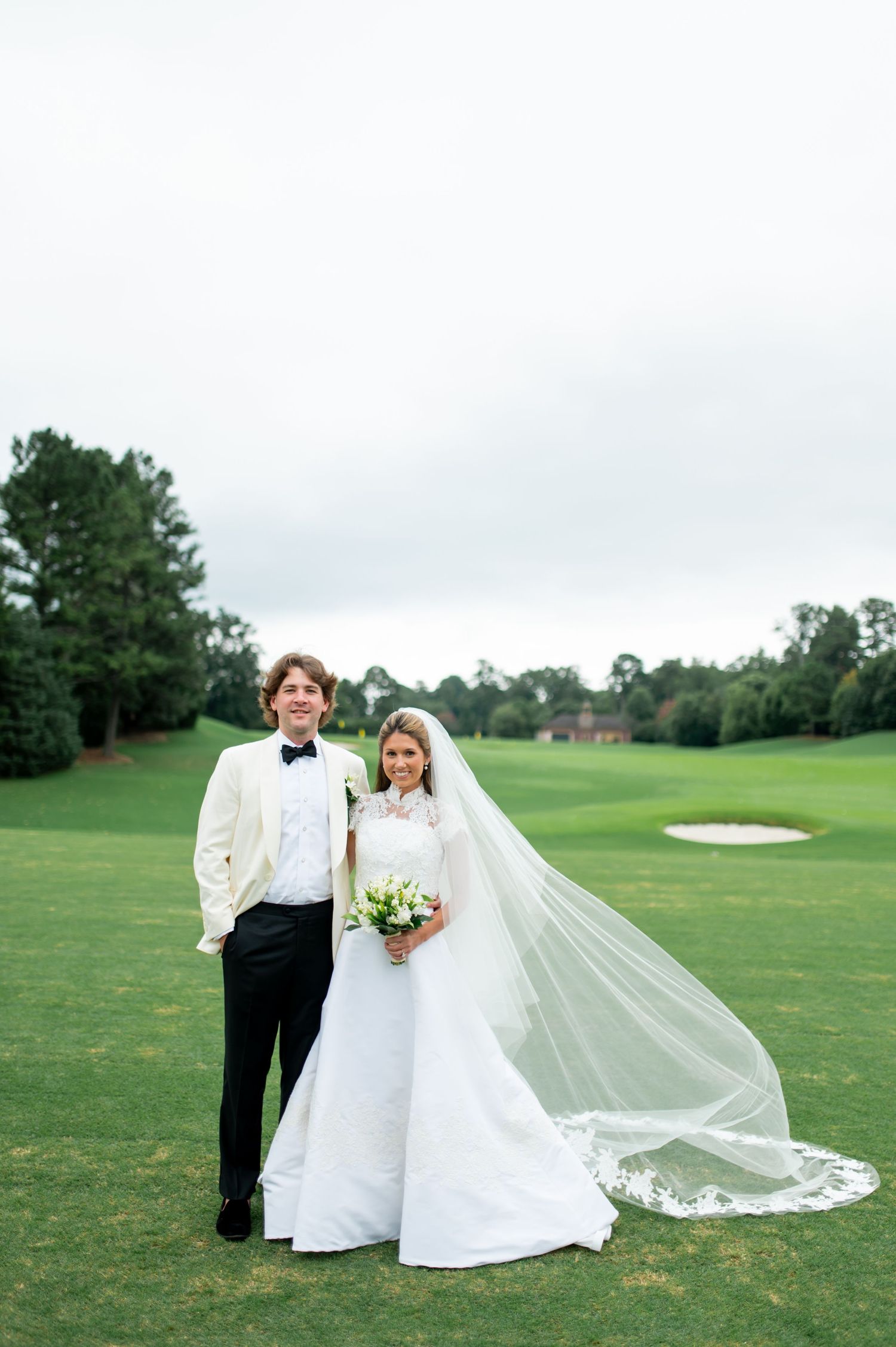 Wedding couple posing on a scenic golf course with a dramatic flowing veil in the breeze.
