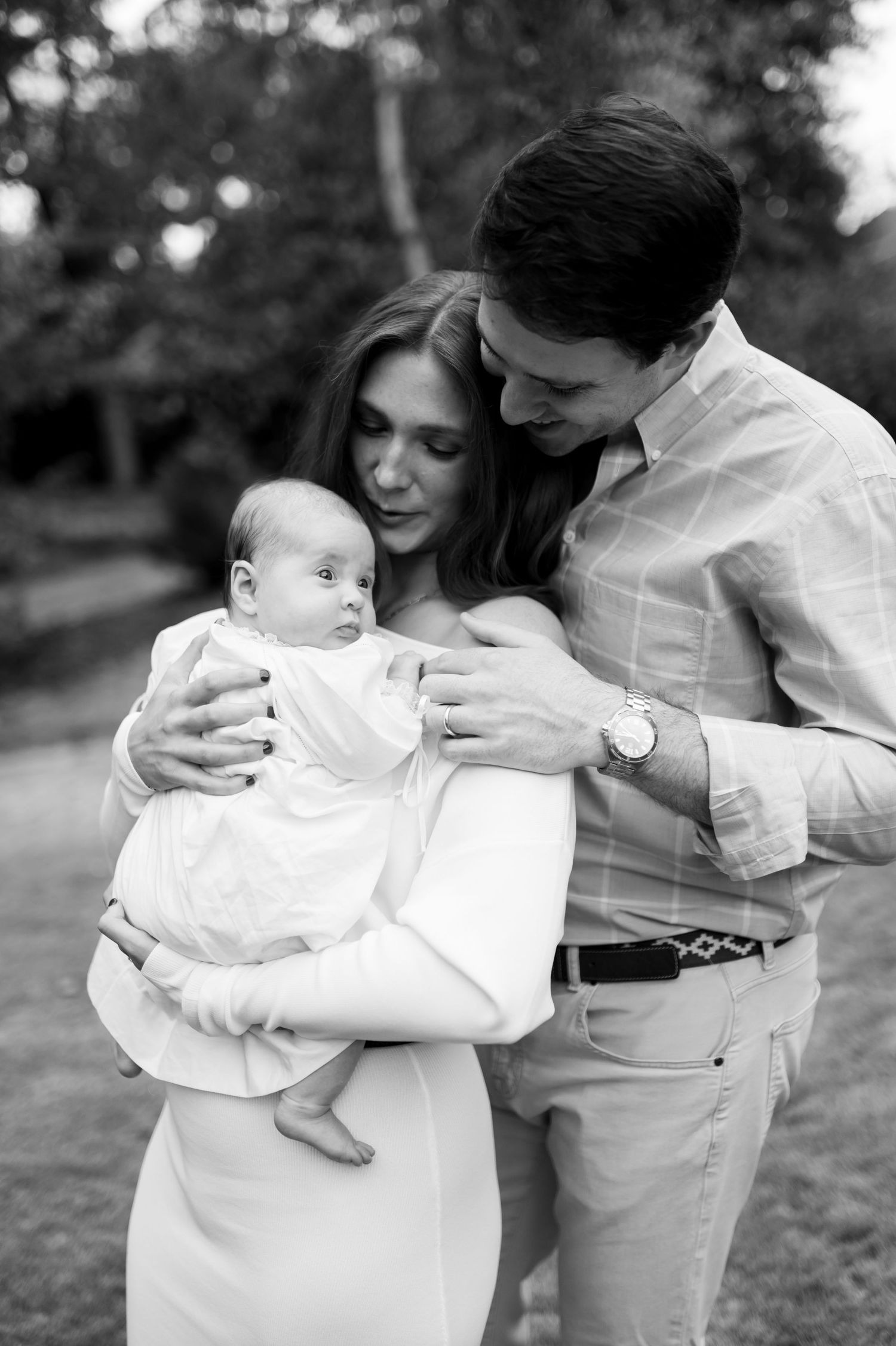 A black and white photo series showing tender moments between parents and their baby outdoors in a park setting.