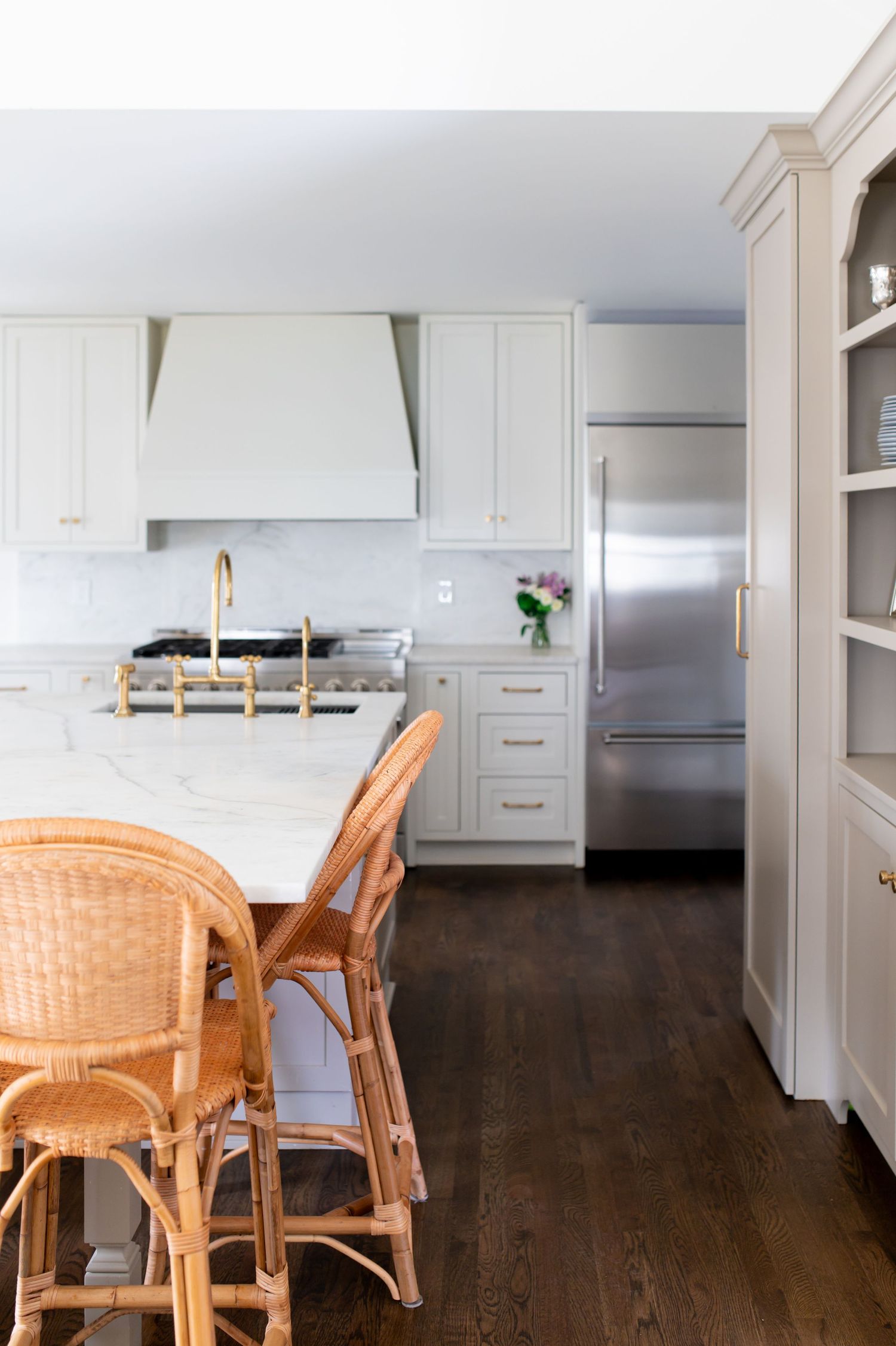 Modern kitchen interior with dark hardwood floors, white cabinets, and rattan dining chairs in an open concept space.