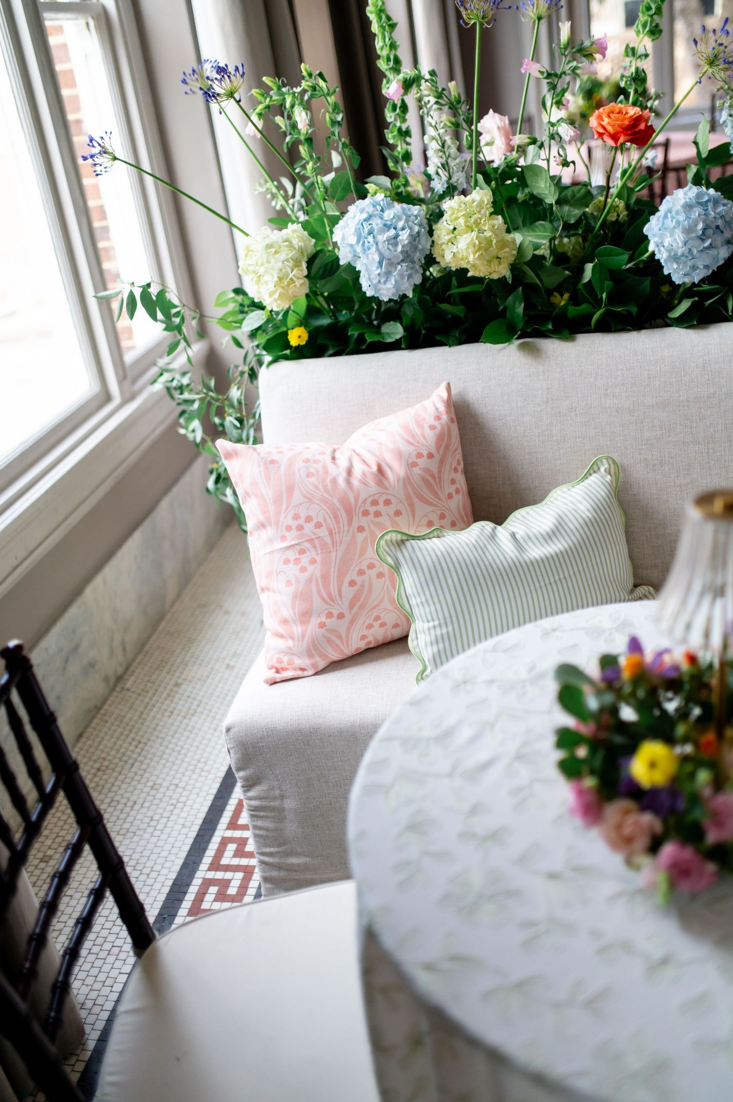 Elegant wedding lounge seating with pink and green patterned pillows, hydrangea floral arrangement by bright windows.