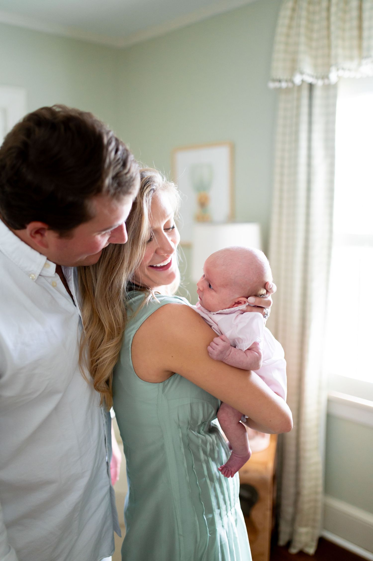 Parents share tender moments with their newborn baby in a sunlit nursery with mint green walls.