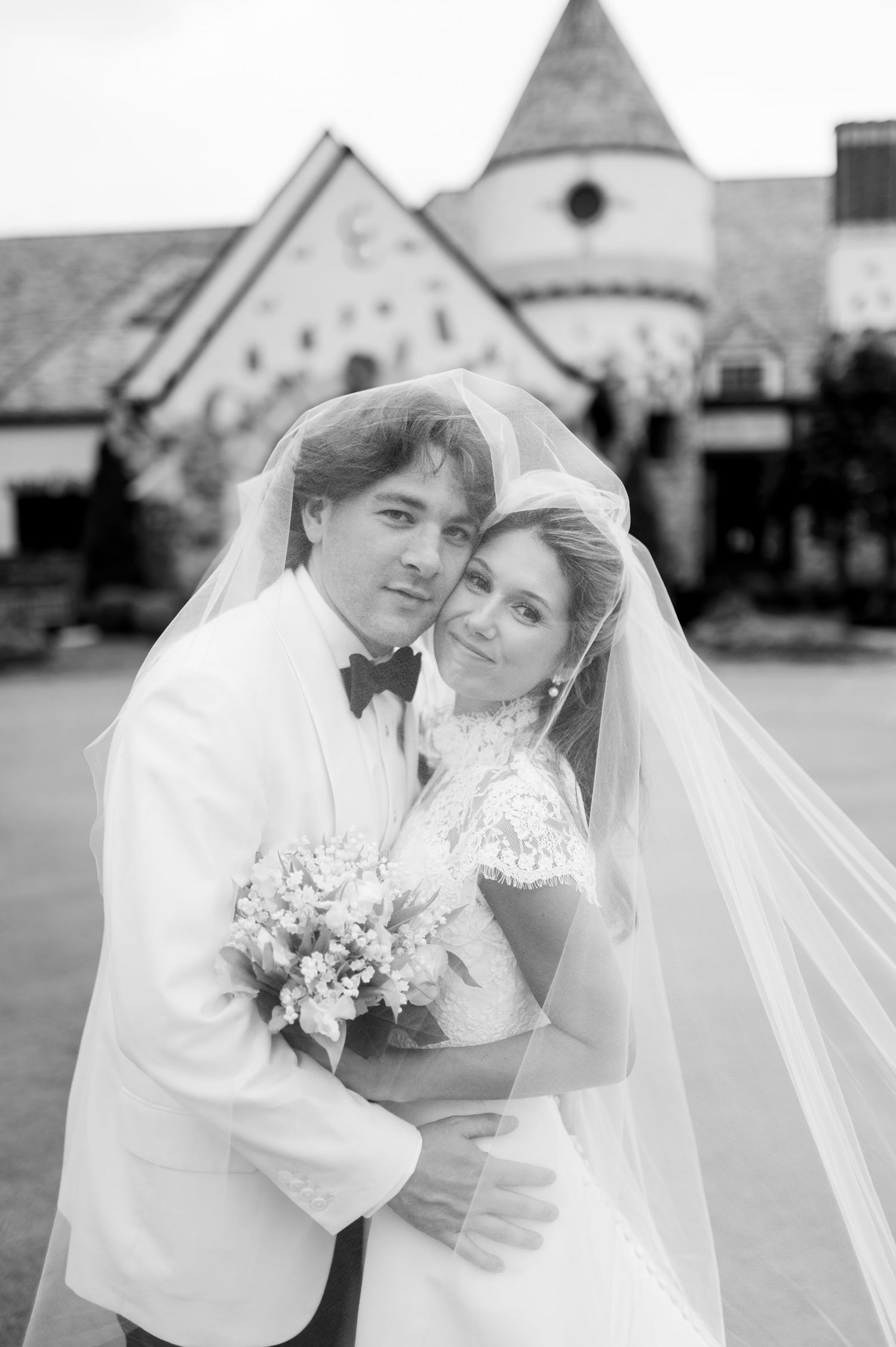 Black and white wedding portrait in front of stone church with classic formal attire.