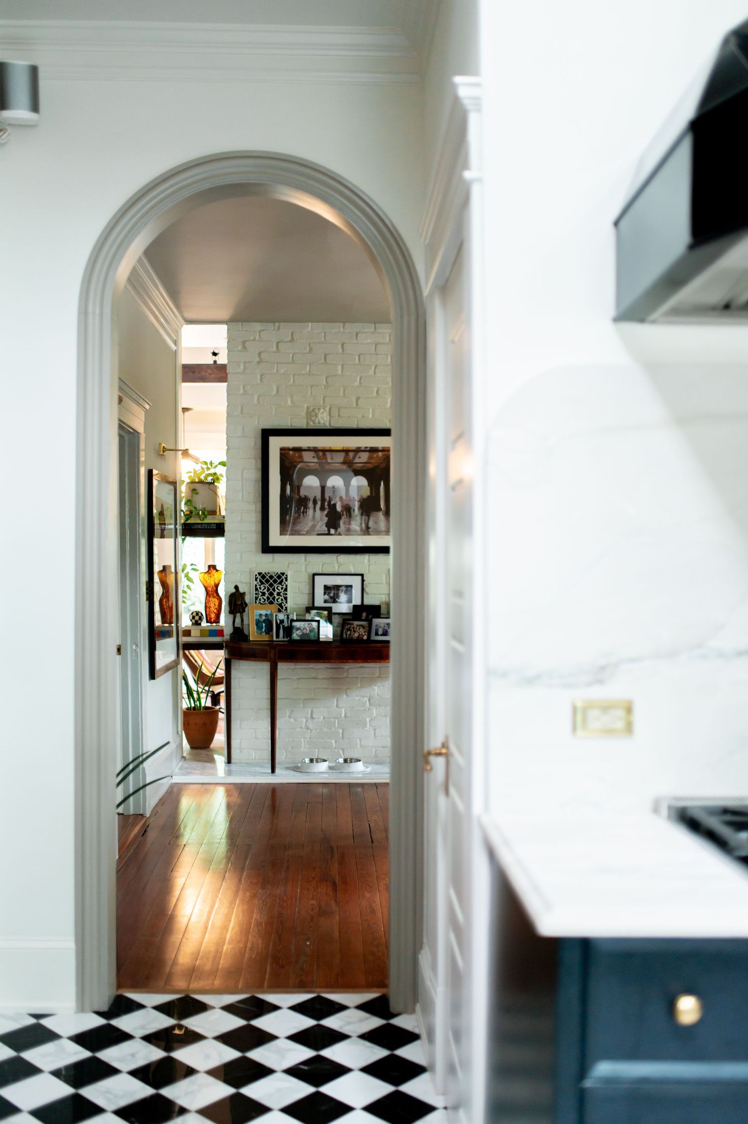 Interior hallway with arched doorways and black and white checkered floor tiles leading to a bright living space.