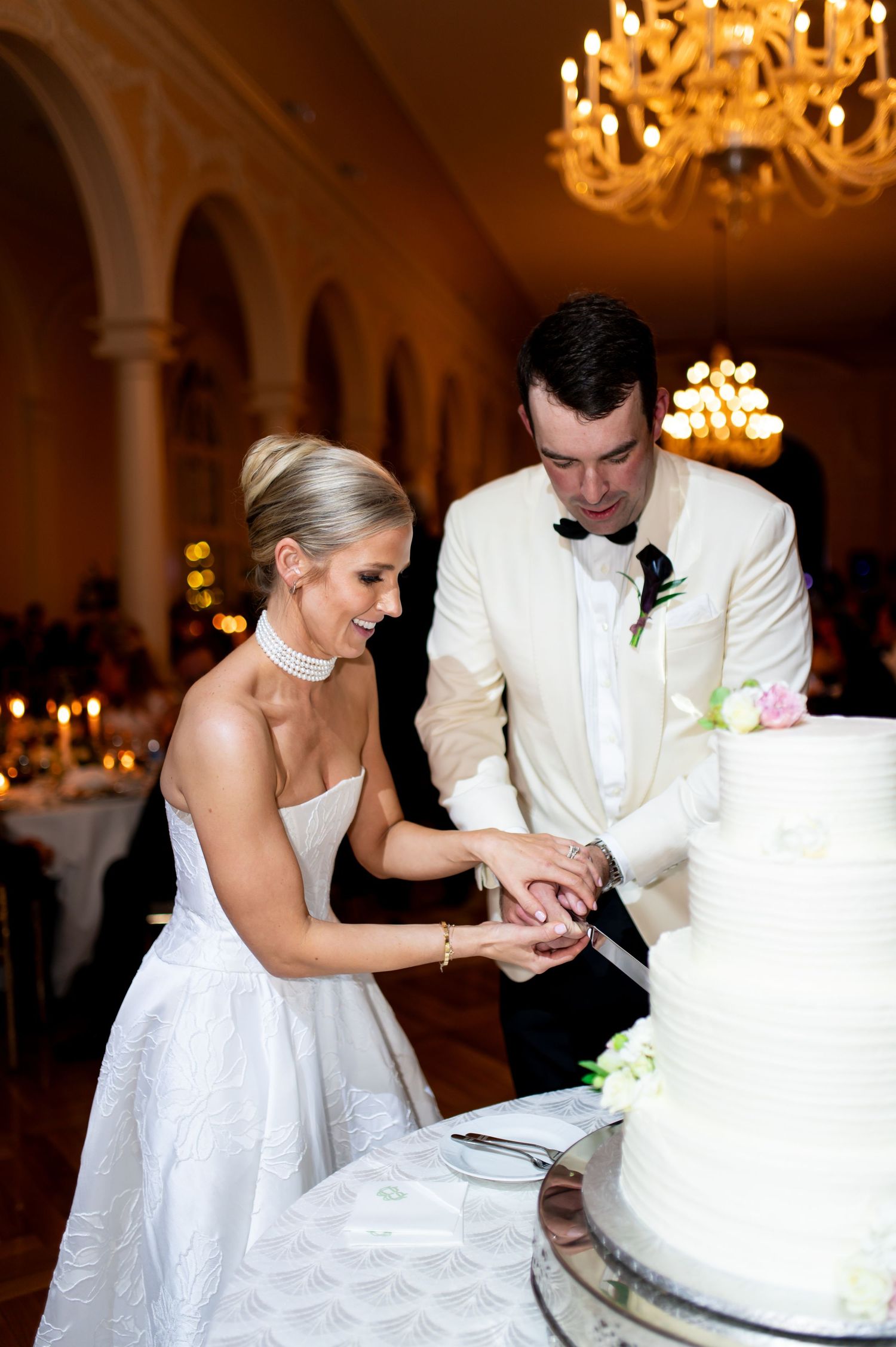 The wedding couple cuts their elegant white tiered cake together at the reception.