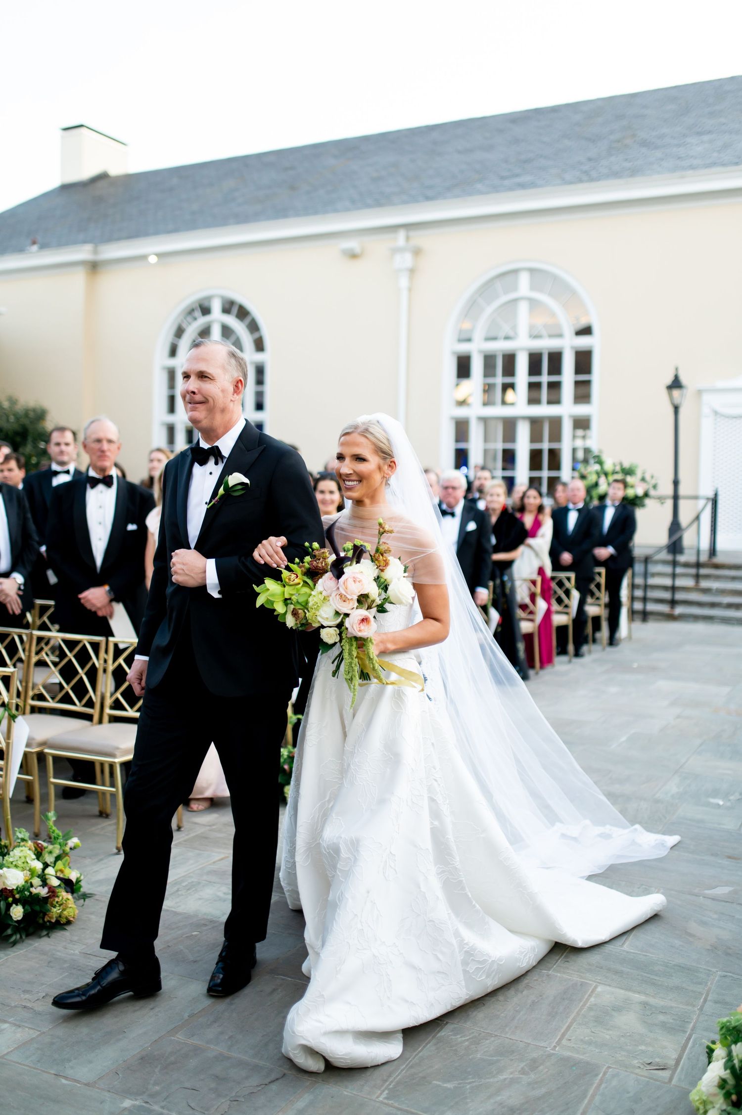 Wedding party poses on stone patio in front of elegant white colonial building.
