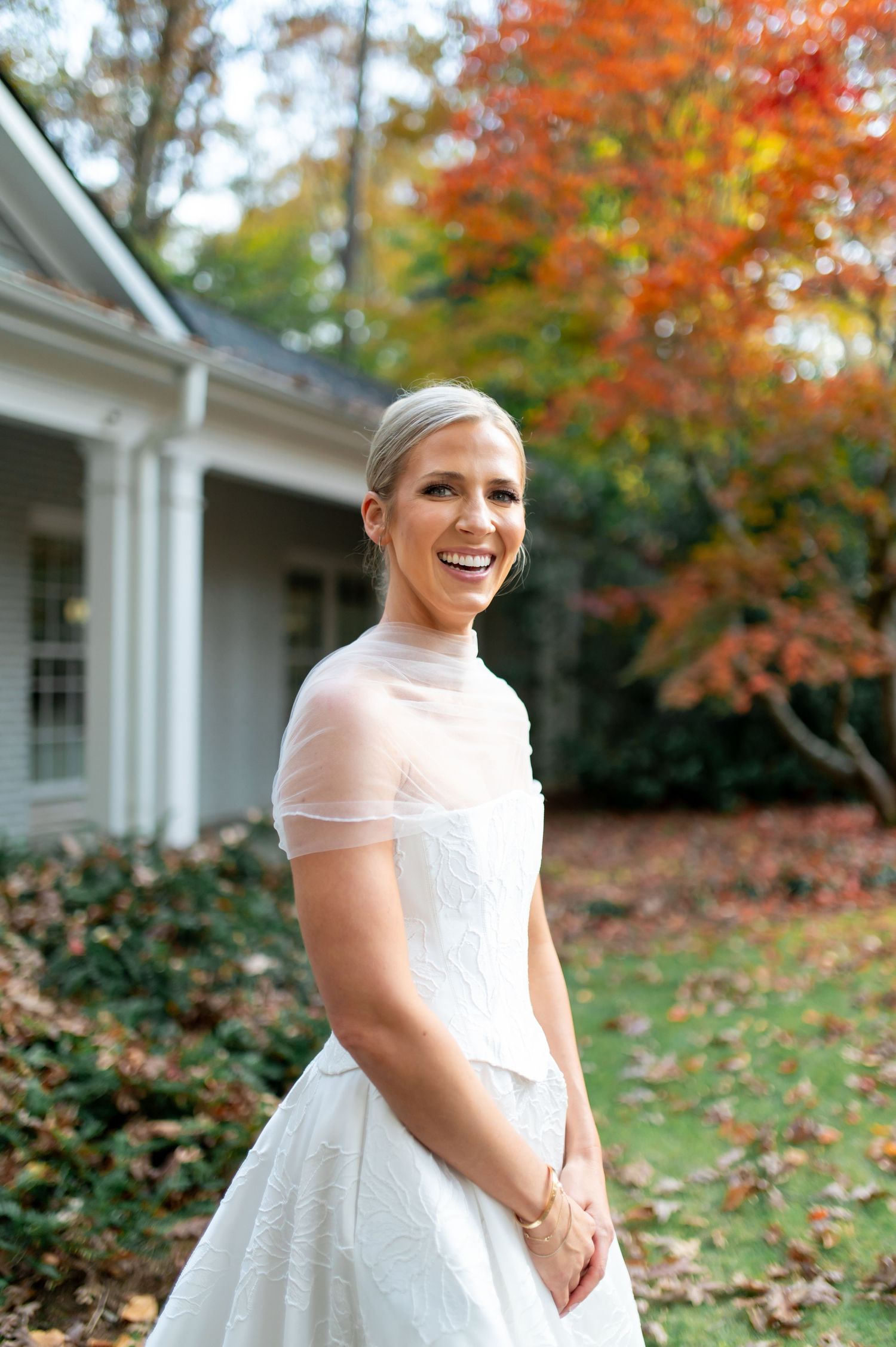 Classic white wedding gown with sheer overlay against vibrant fall foliage.