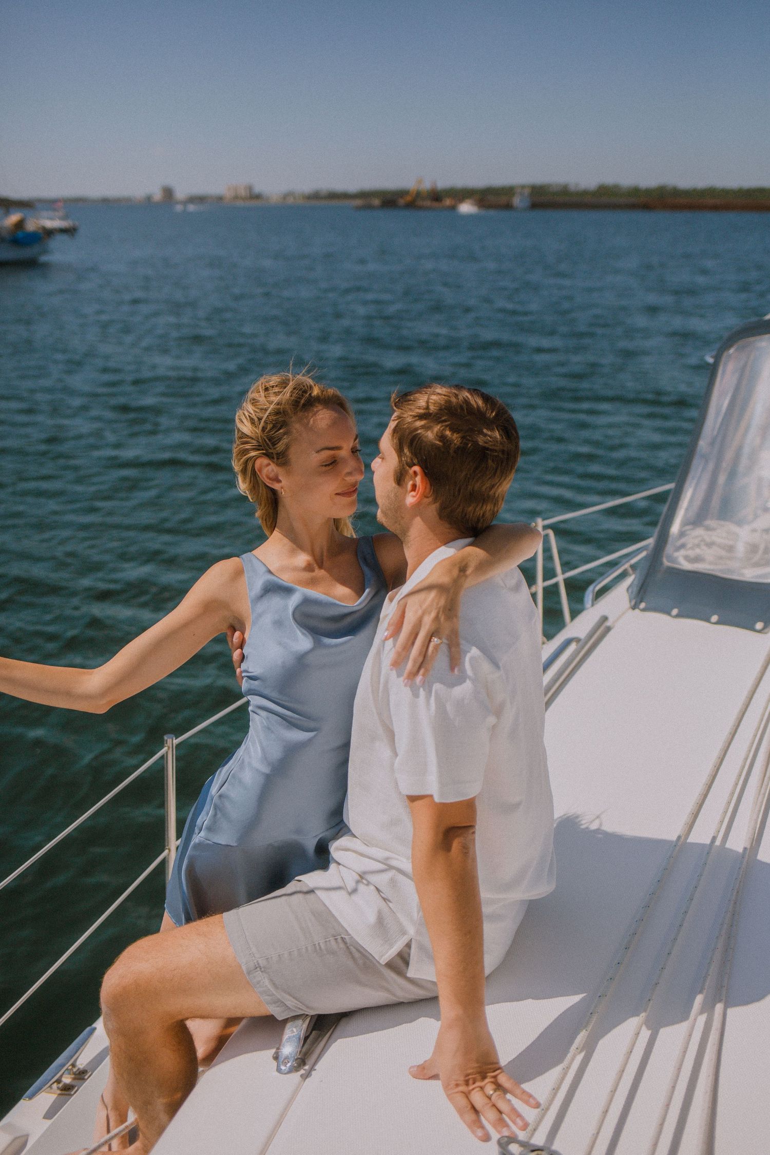 Couple sitting together on yacht railing, gazing at each other on a sunny summer day.