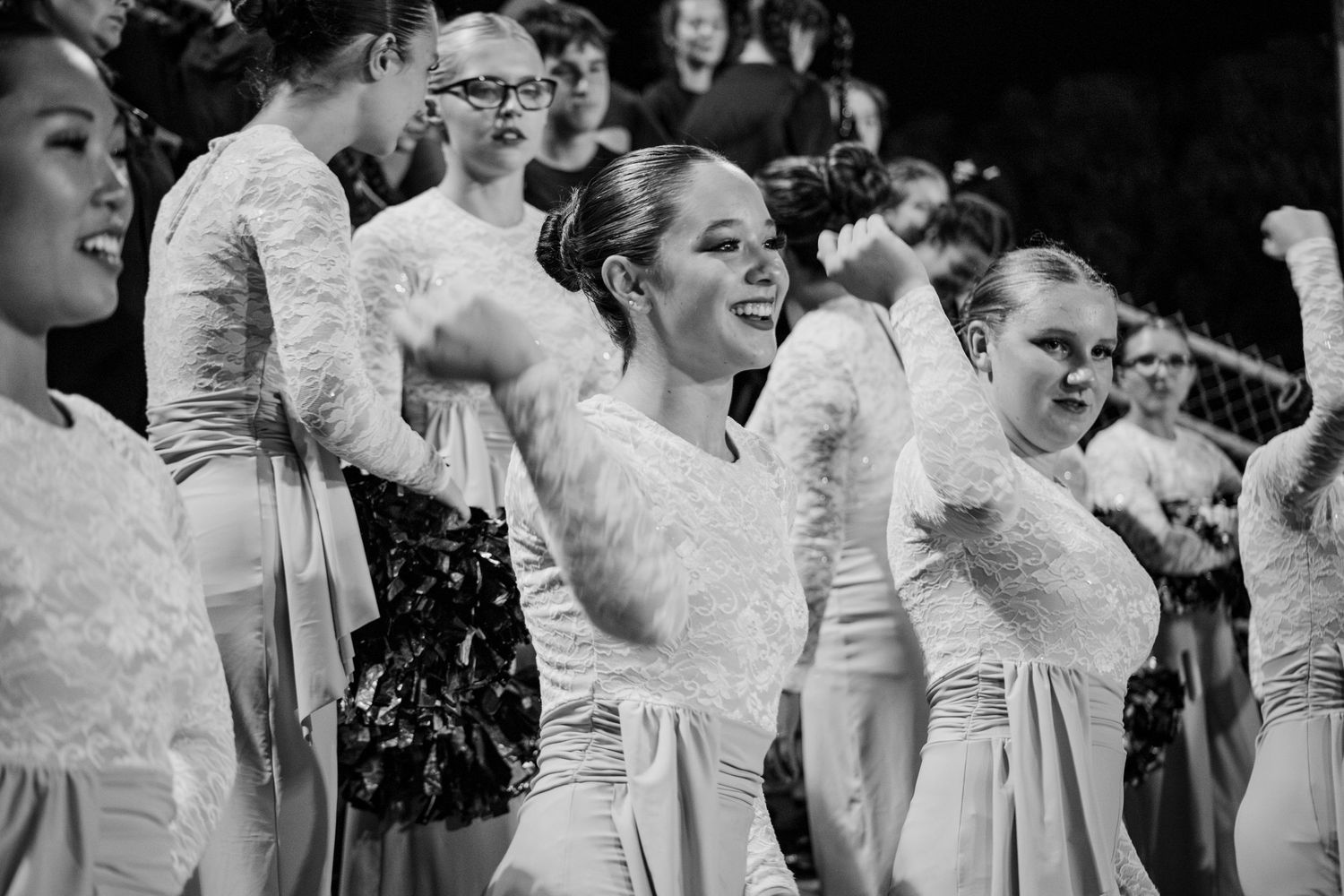 Black and white photo of smiling women in white dresses performing a dance routine at a group event.