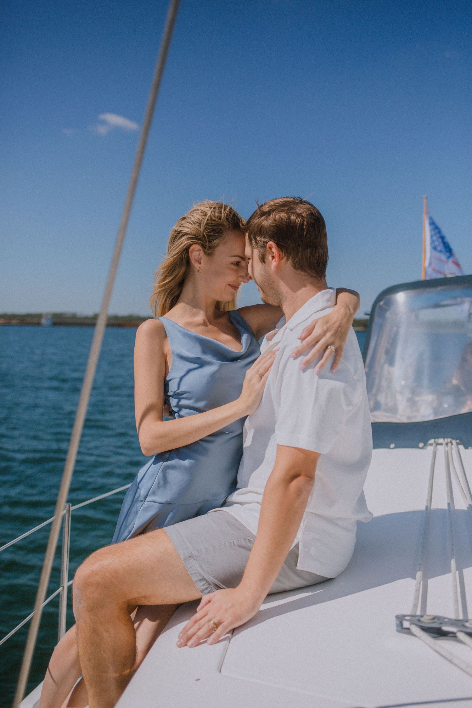 Couple embracing nose-to-nose on a white sailboat on a sunny day.