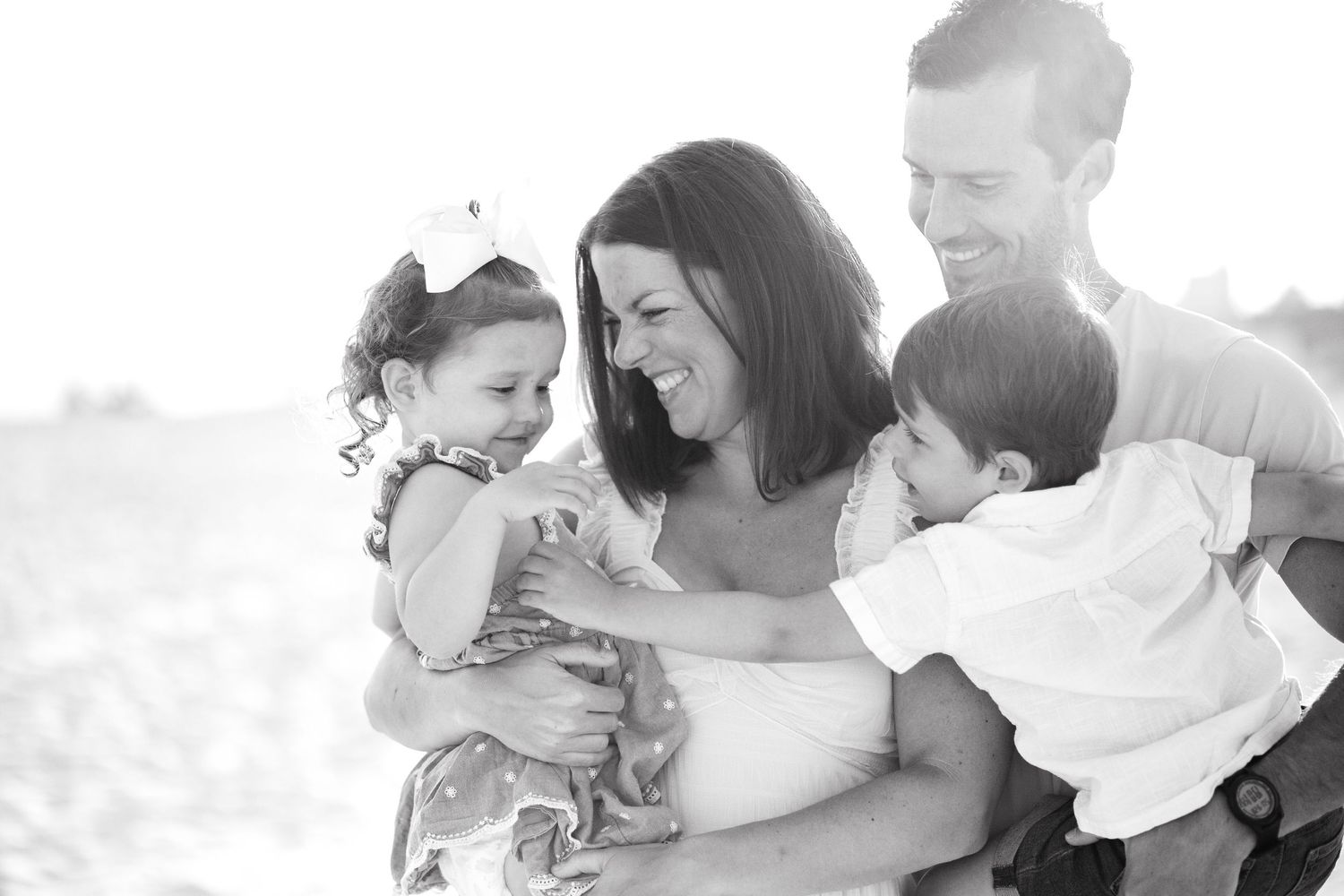 Black and white photo of a happy family with two young children at the beach.