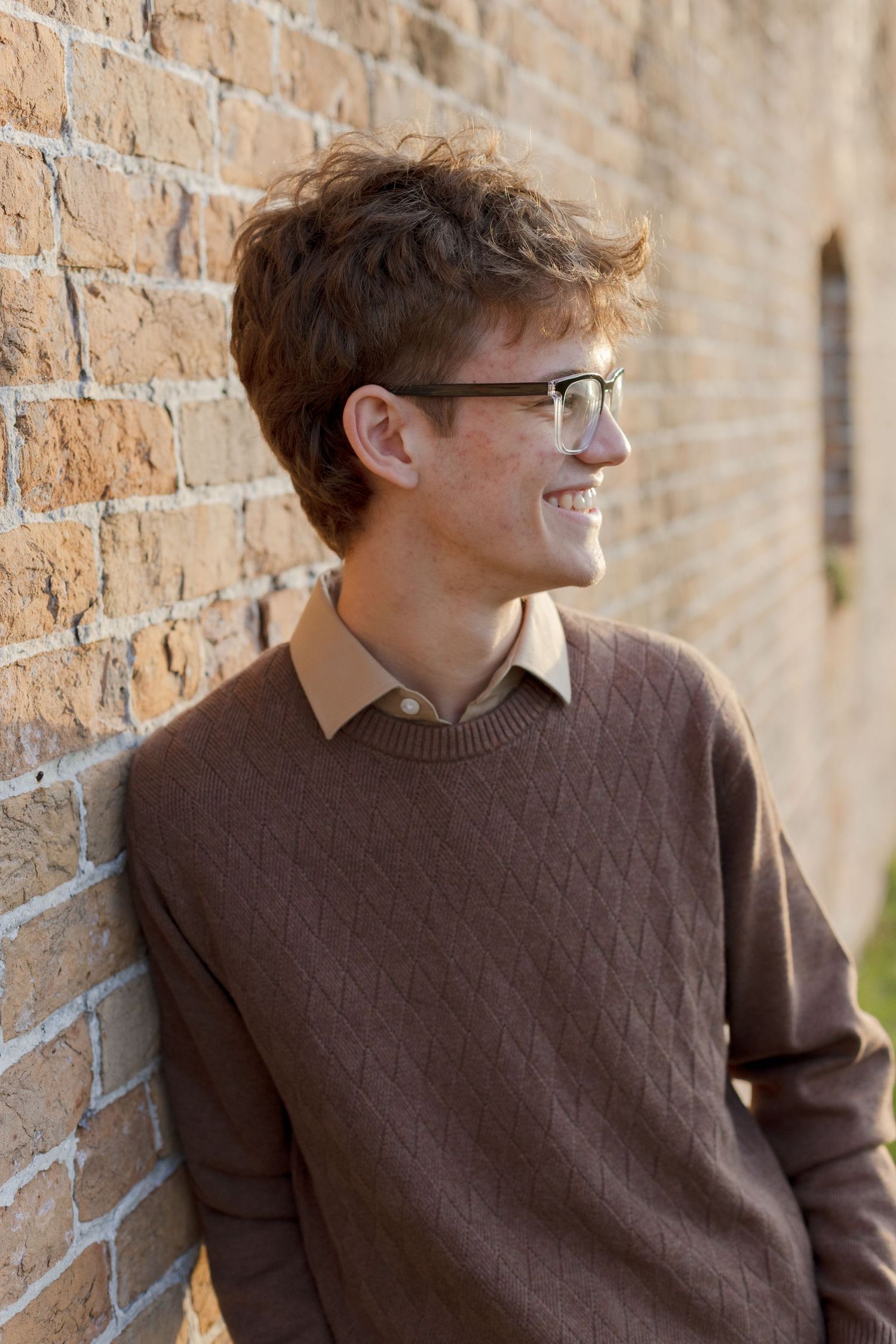 young man leaning against a brick wall in setting sunlight