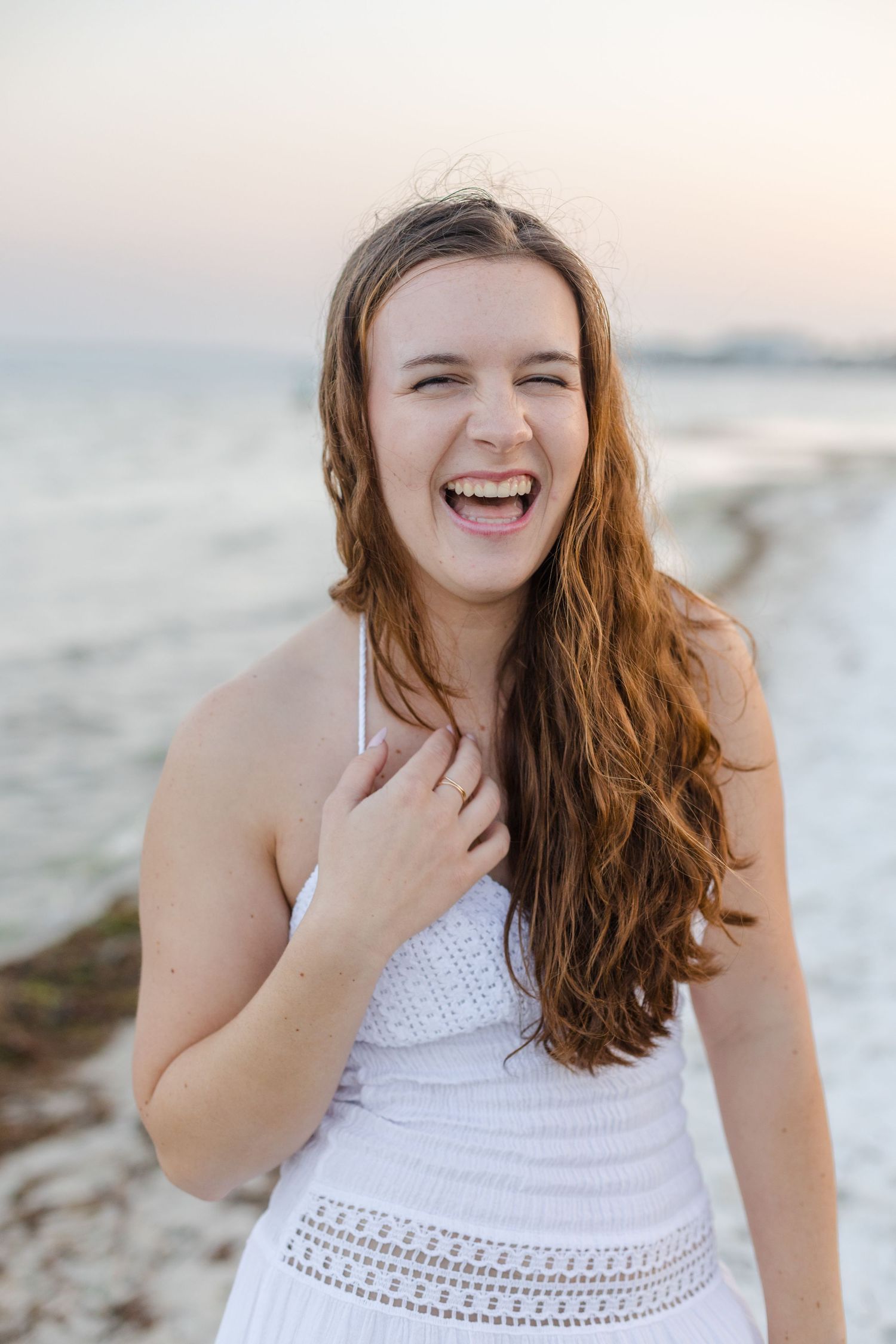 Laughing teenage girl in a white dress enjoying a fun beach photo session.